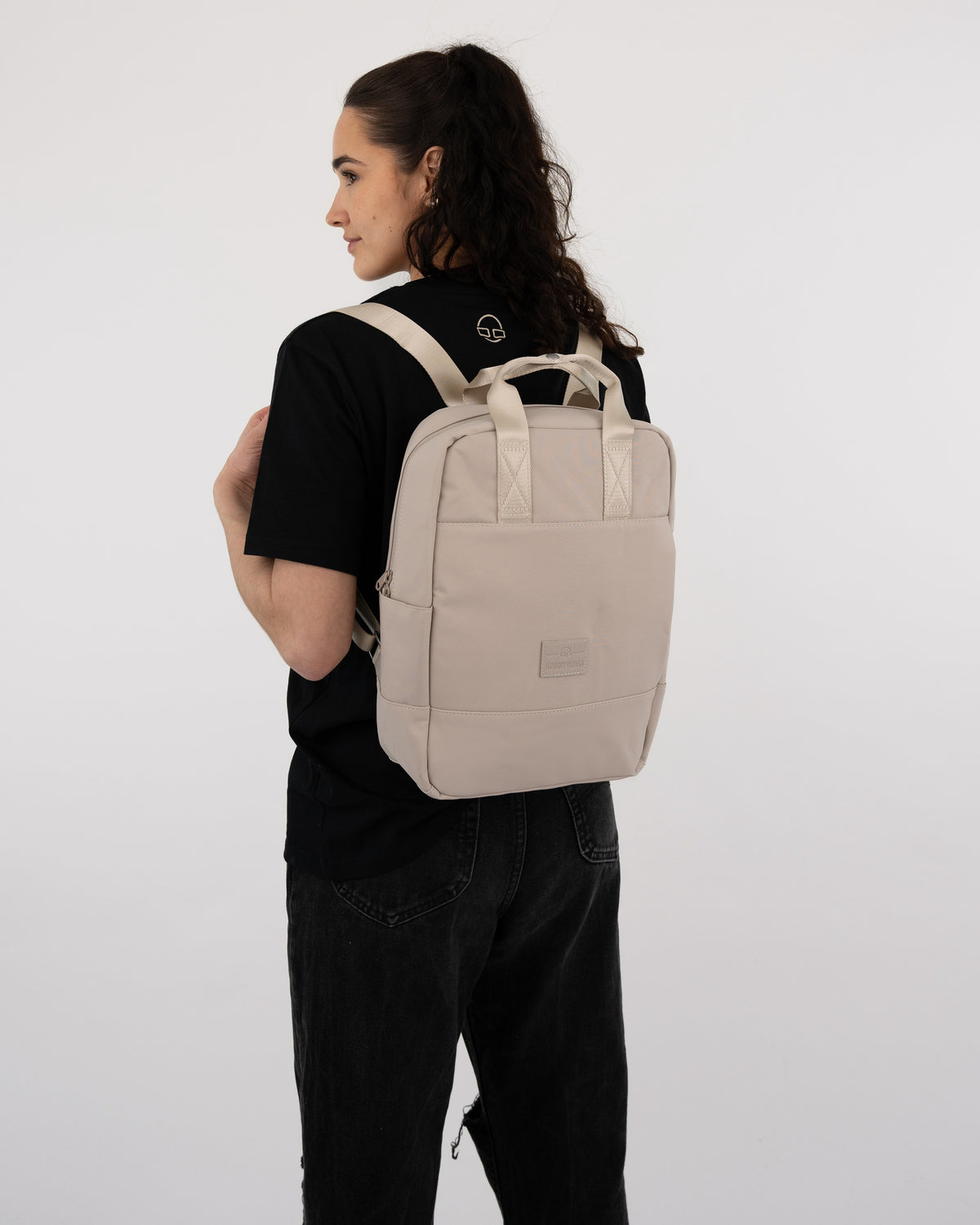 Frau mit beigem Johnny Urban Rucksack 'Jona Medium' und schwarzem T-Shirt und Hose