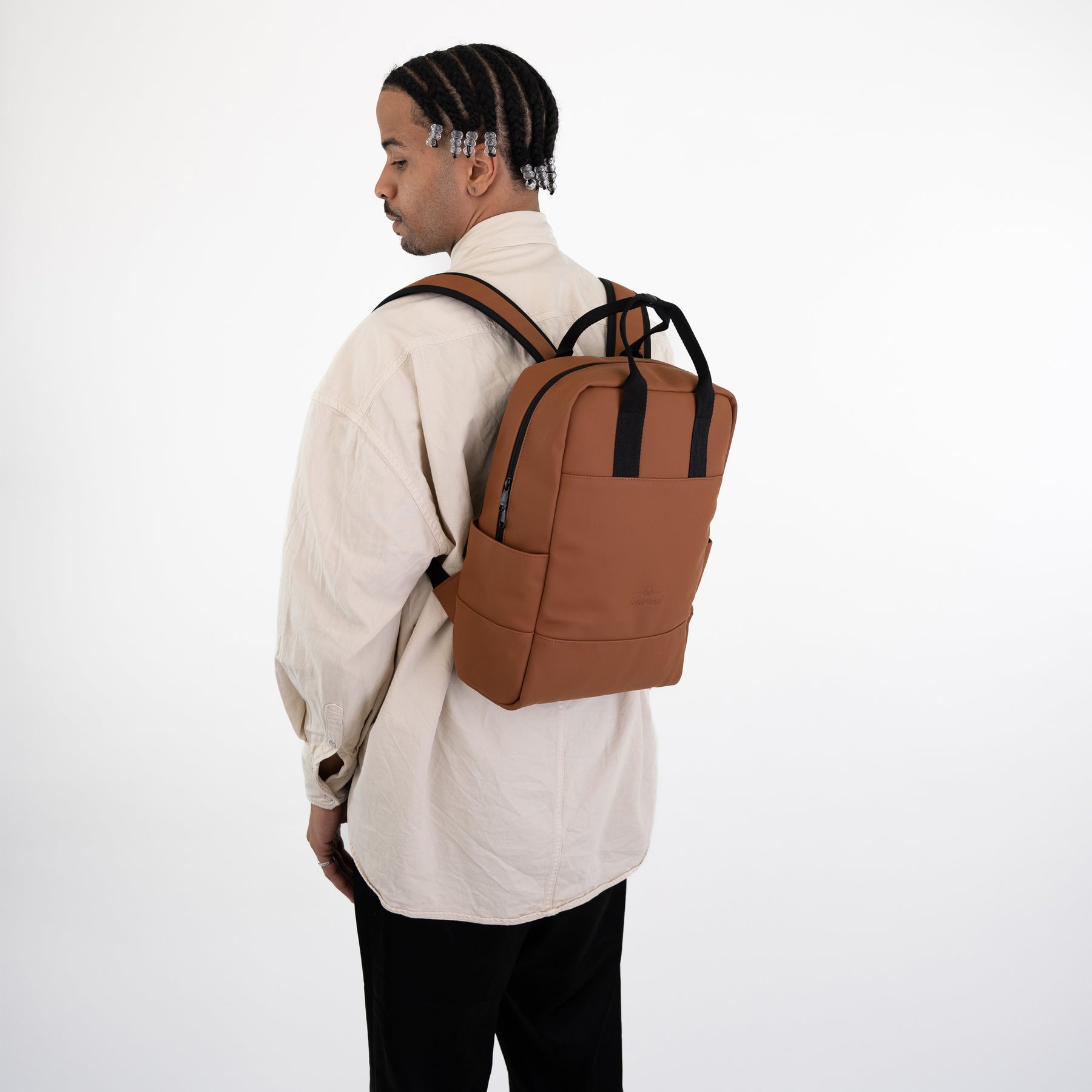 Mann von hinten mit hellbeiger Hemdjacke trägt braunen Johnny Urban Rucksack 'Hailey' mit schwarzen Tragegriffen und Schultergurten