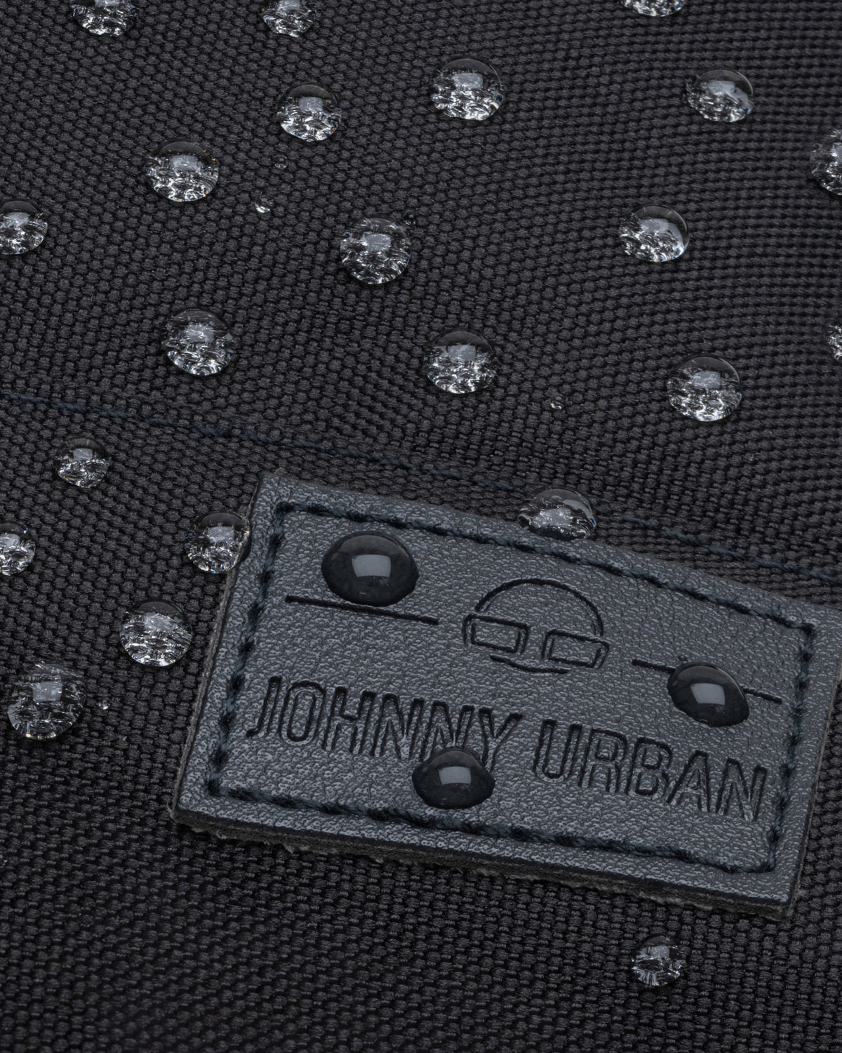 Nahaufnahme von wasserdichten Regentropfen auf dem schwarzen Stoff des Damenrucksacks 'Mia' von Johnny Urban