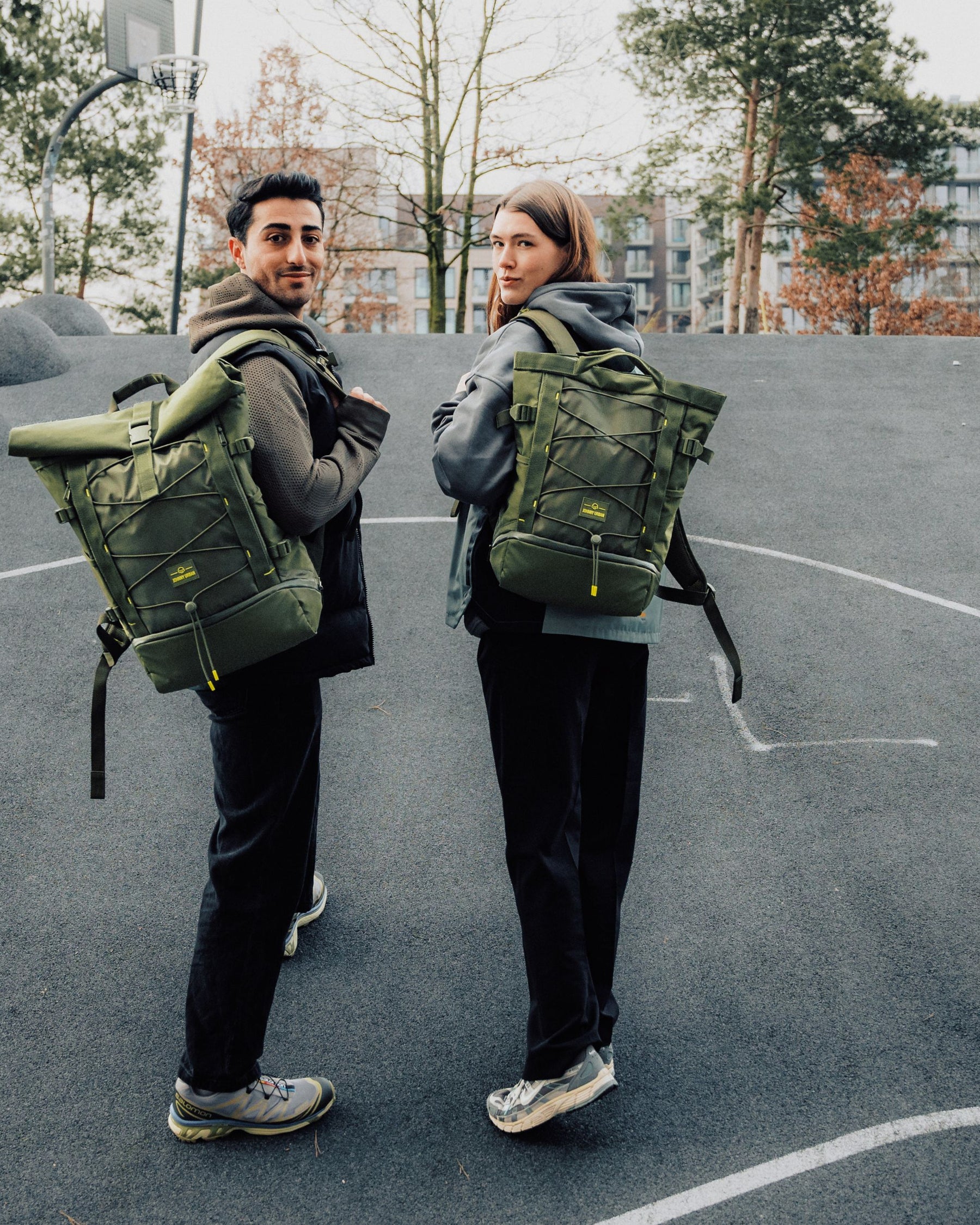 Zwei Personen, jeweils mit olivgrünem Rucksack 'Harper', auf einem urbanen Basketballplatz