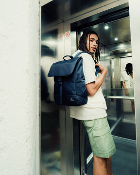 Mann mit Dreadlocks trägt schwarzen Johnny Urban Rucksack 'Mika' und steht in einem Aufzug