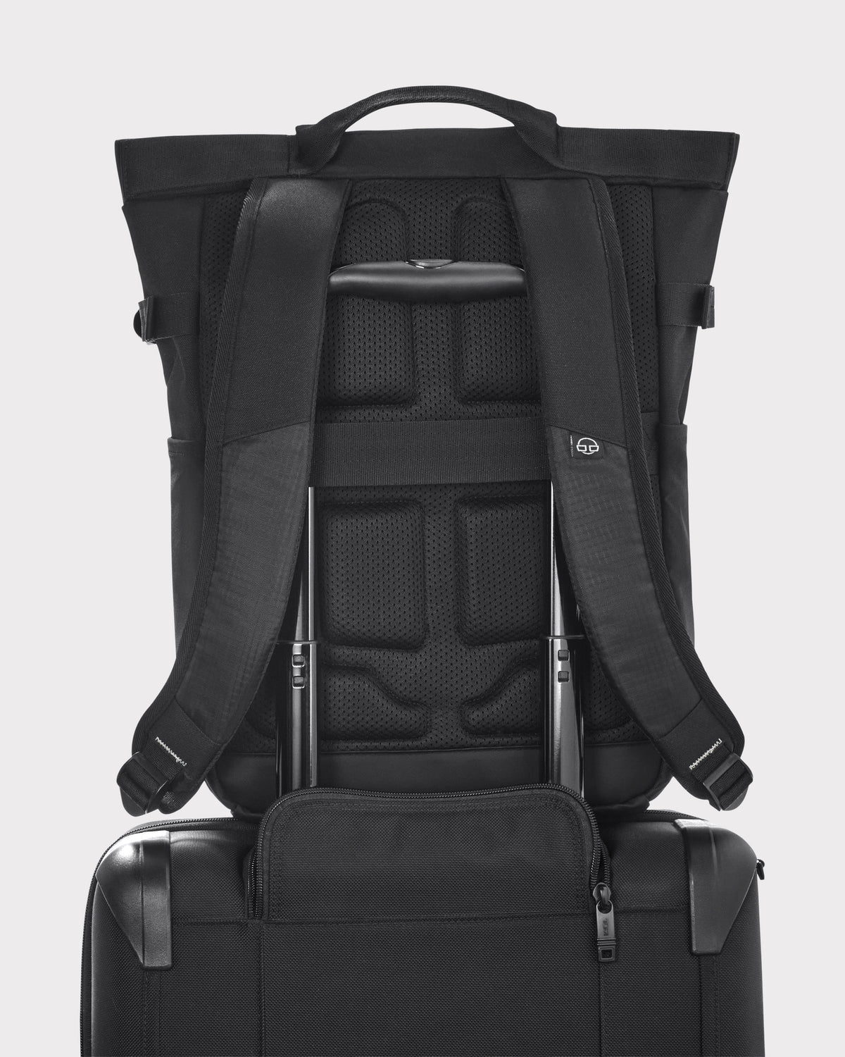 Schwarzer Rucksack 'Harper' von Johnny Urban auf einem schwarzen Trolley befestigt, gezeigt von hinten mit gepolstertem Rücken und verstellbaren Schultergurten