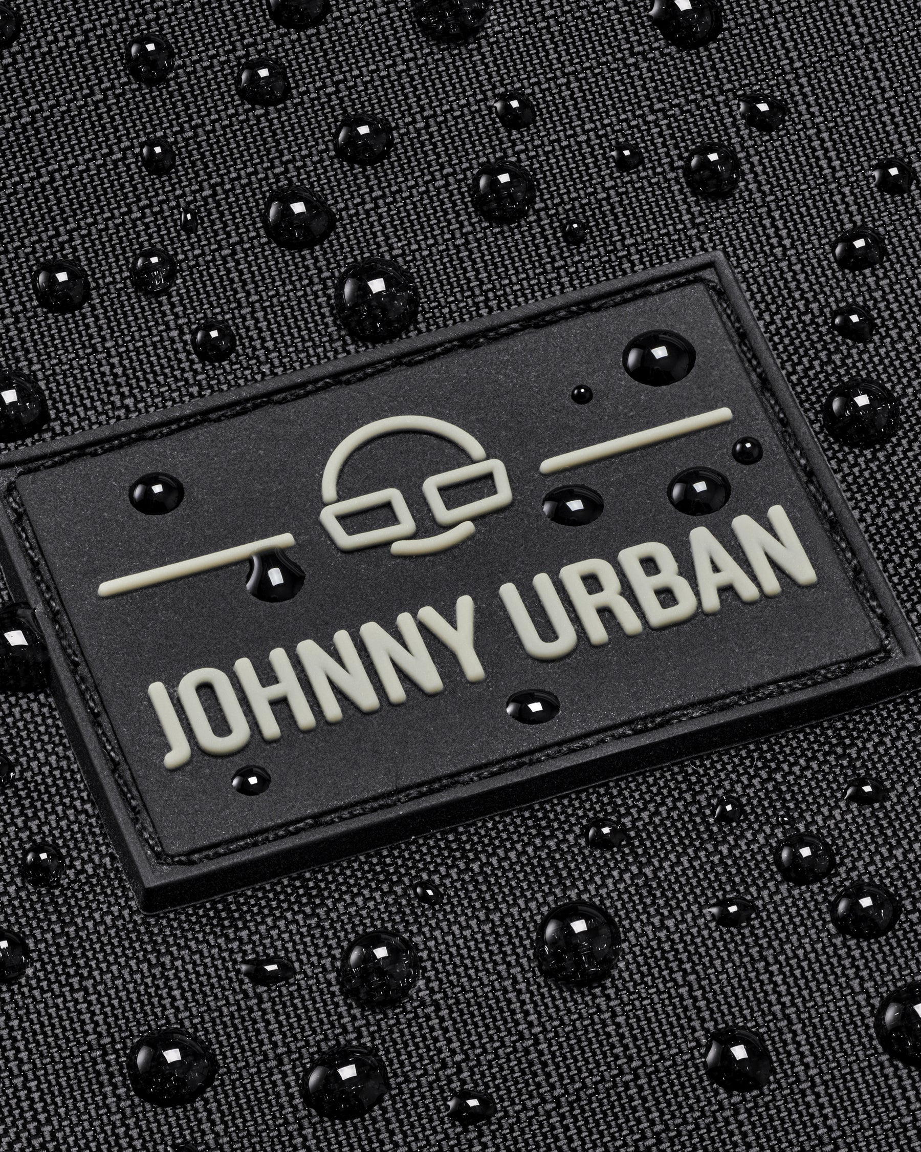 Nahe Aufnahme des Johnny Urban Logos auf einem wasserabweisenden schwarzen Gewebe mit Wassertropfen