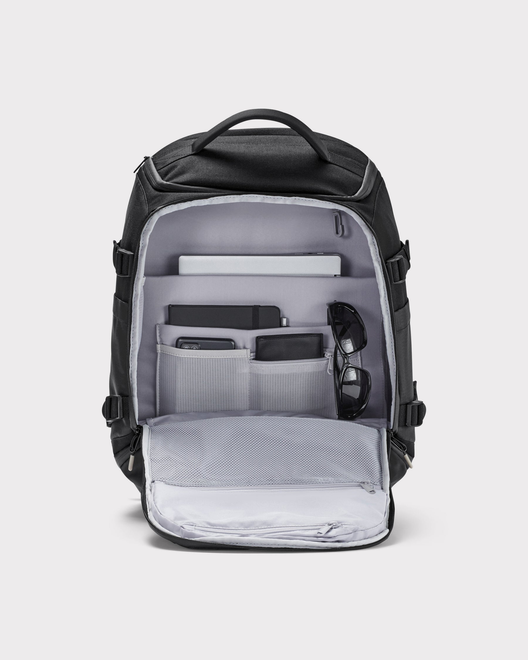 Schwarzer Rucksack 'Jack' von Johnny Urban mit mehreren Fächern, geöffnet und bestückt mit Notebook, Notizbuch, Smartphone, Geldbörse und Sonnenbrille