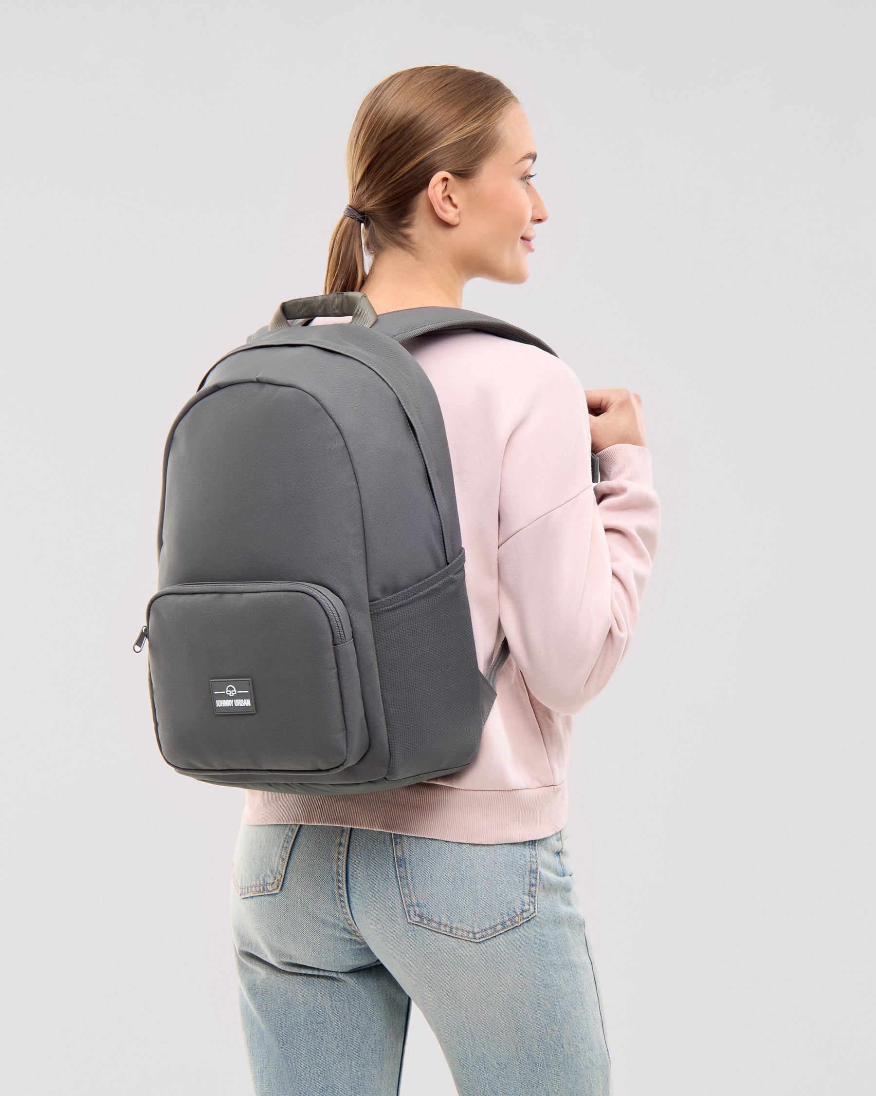 Frau trägt dunkelgrauen Rucksack 'Mo' von Johnny Urban, rosa Pullover, blaue Jeans