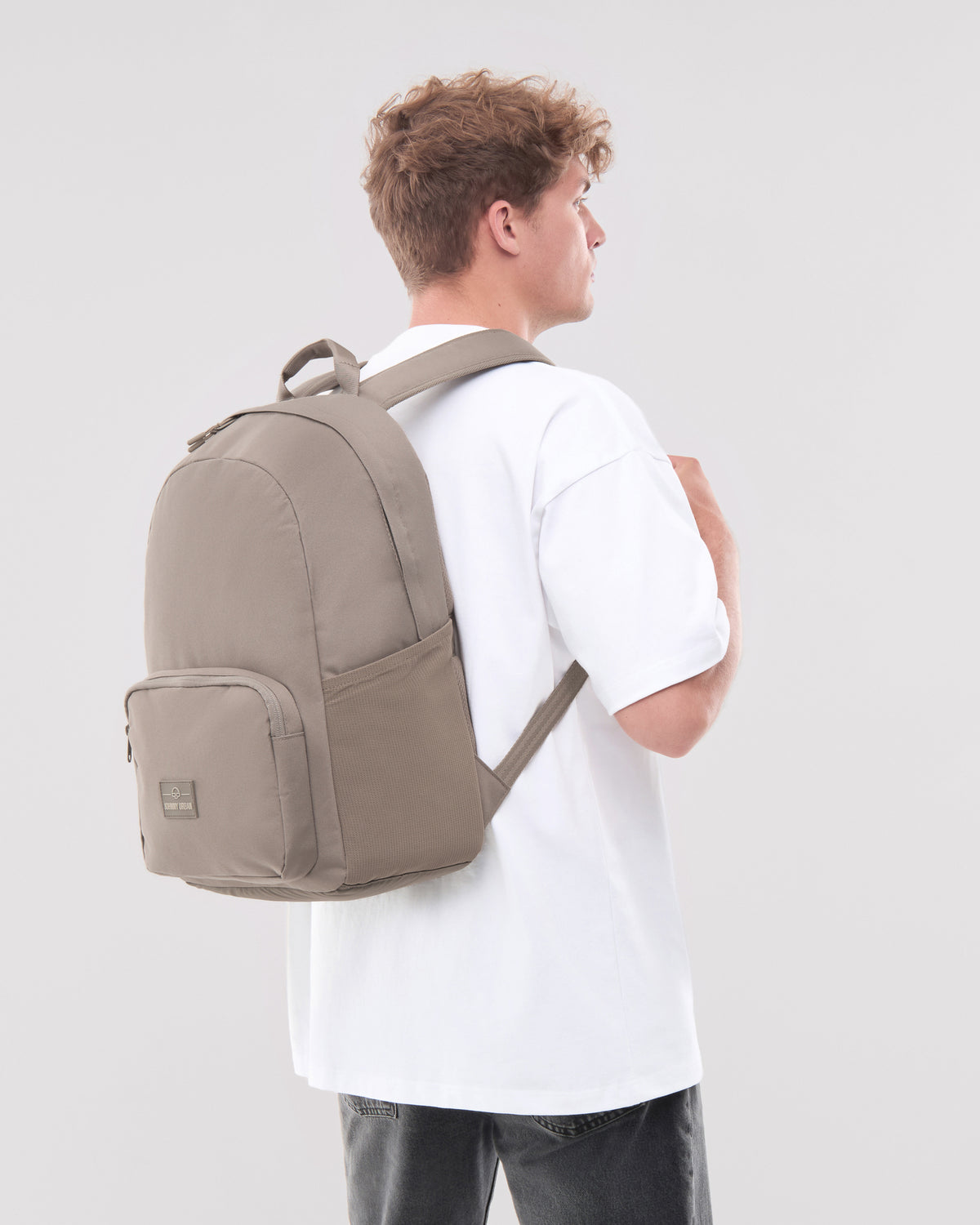 Mann in weißem T-Shirt trägt urbanen 'Mo' Rucksack in desert grey