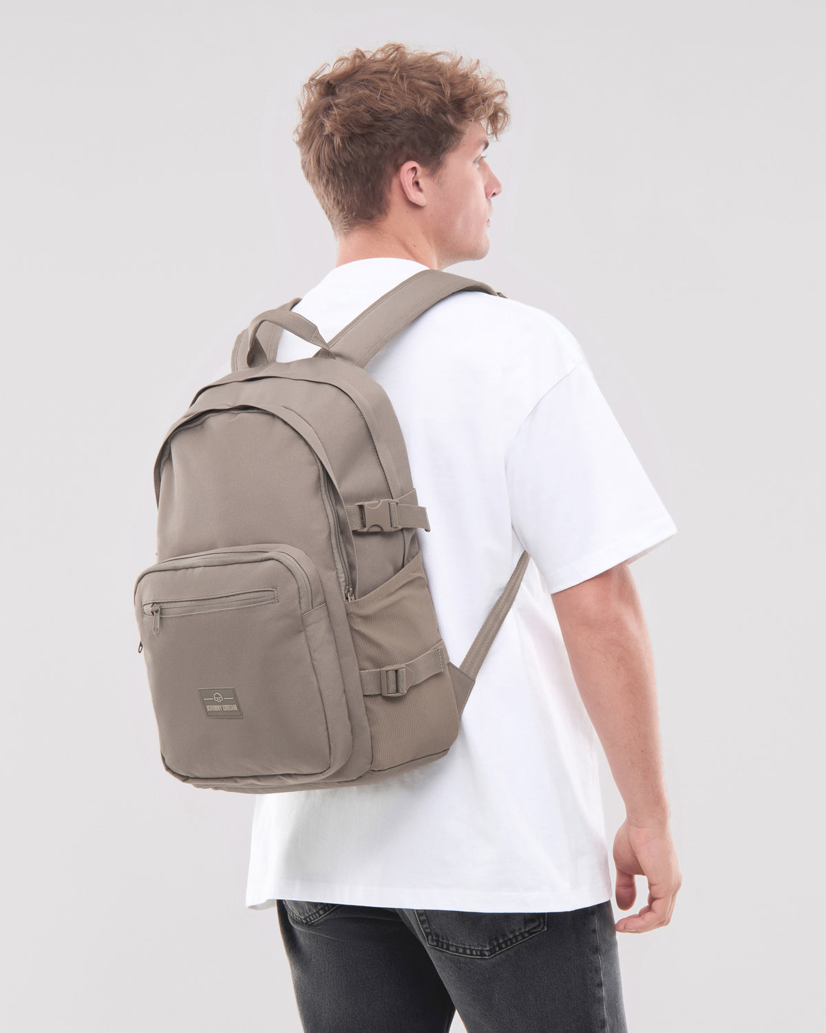 Herren trägt Rucksack 'Lian' in desert-grau auf weißem T-Shirt und schwarzen Jeans