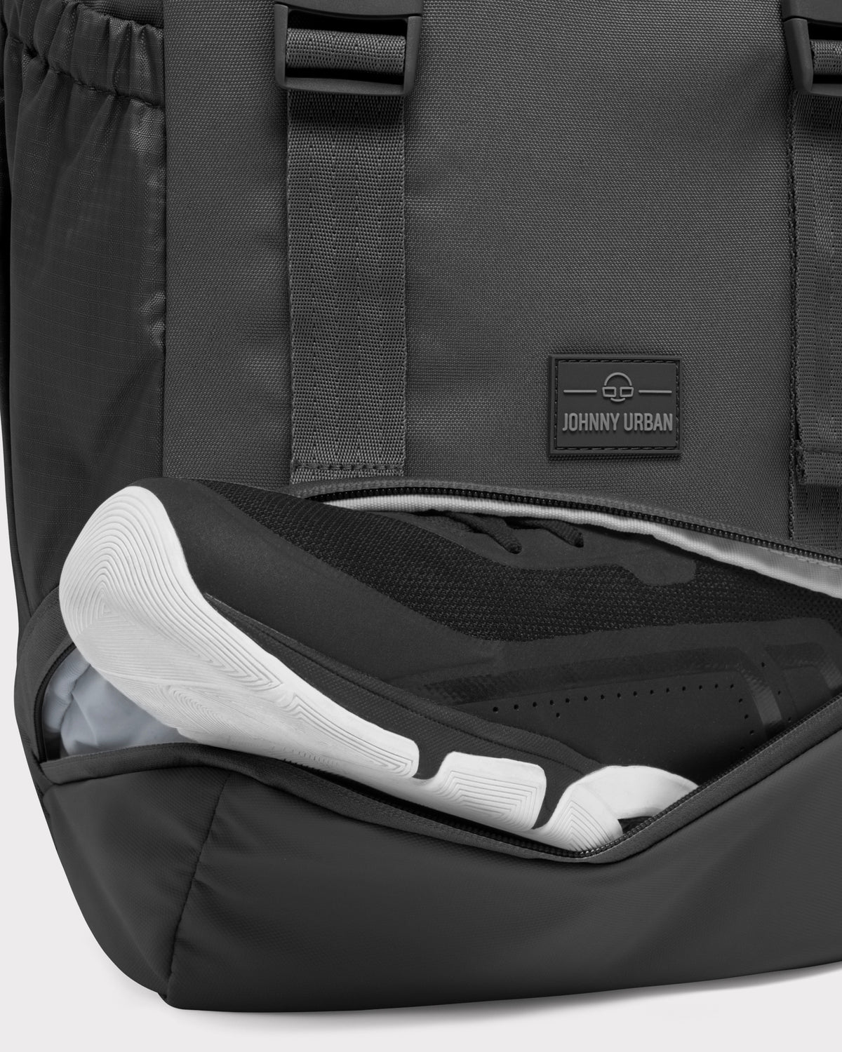 Schwarzer Johnny Urban Rucksack 'Nico' mit offenem Schuhfach, das einen schwarzen Sportschuh mit weißer Sohle enthält