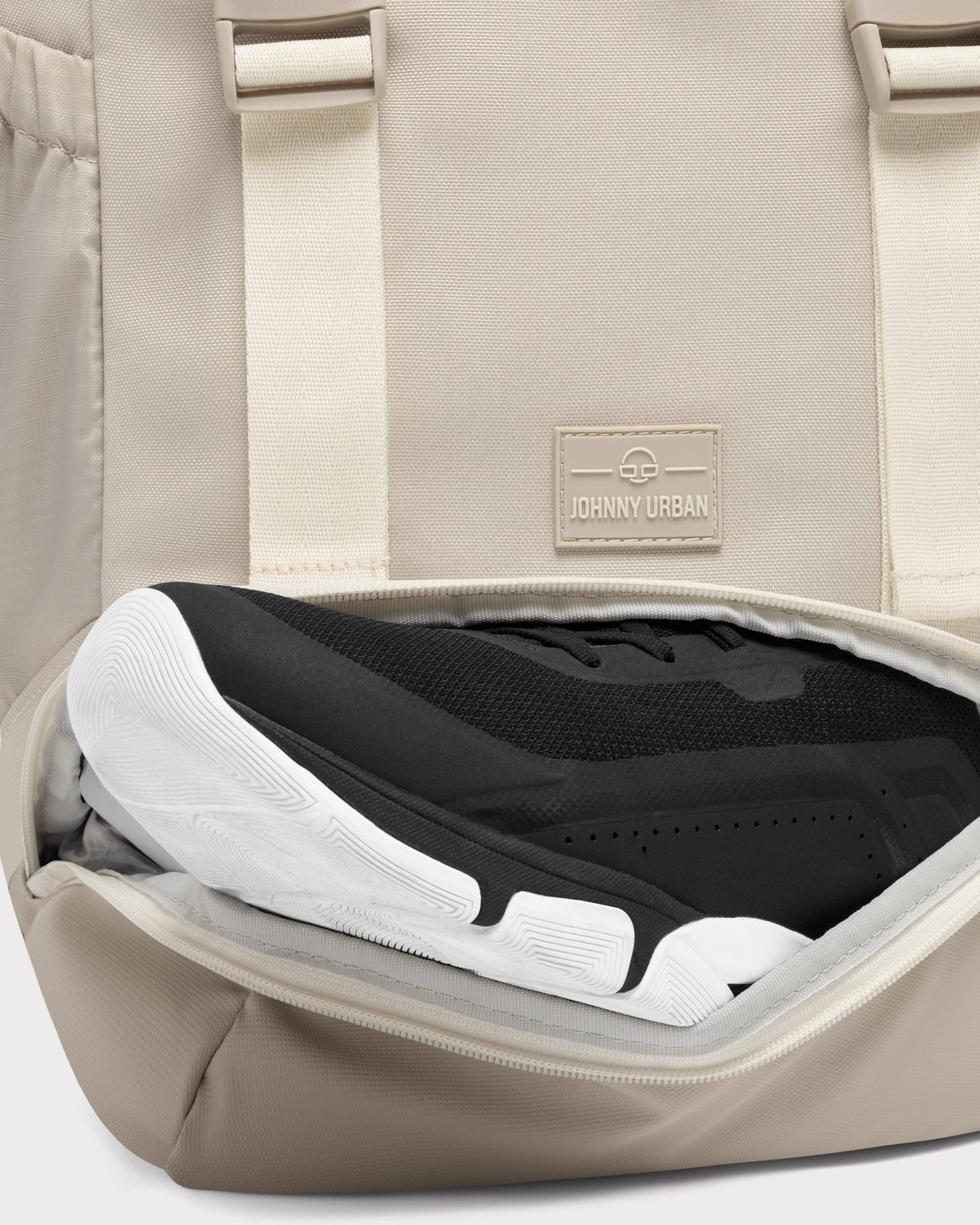 Beiger Johnny Urban Rucksack 'Nico' mit unterem Reißverschlussfach, das einen schwarzen Sportschuh zeigt