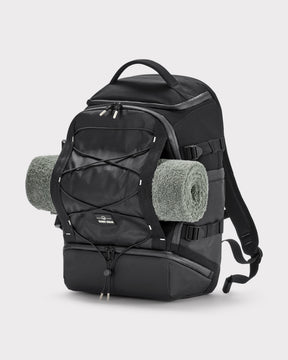 Schwarzer Johnny Urban Rucksack 'Jack' aus robustem Material mit aufgerolltem grauen Handtuch an der Außenseite