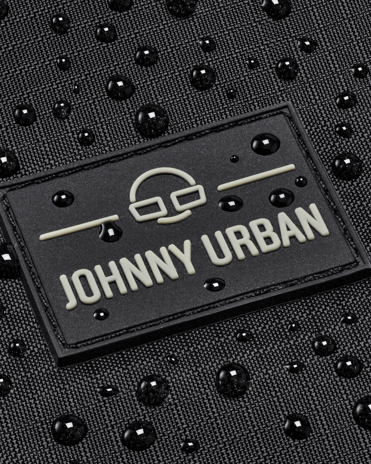 Logo-Patch von Johnny Urban auf wasserabweisendem schwarzen Rucksackmaterial mit Wassertropfen