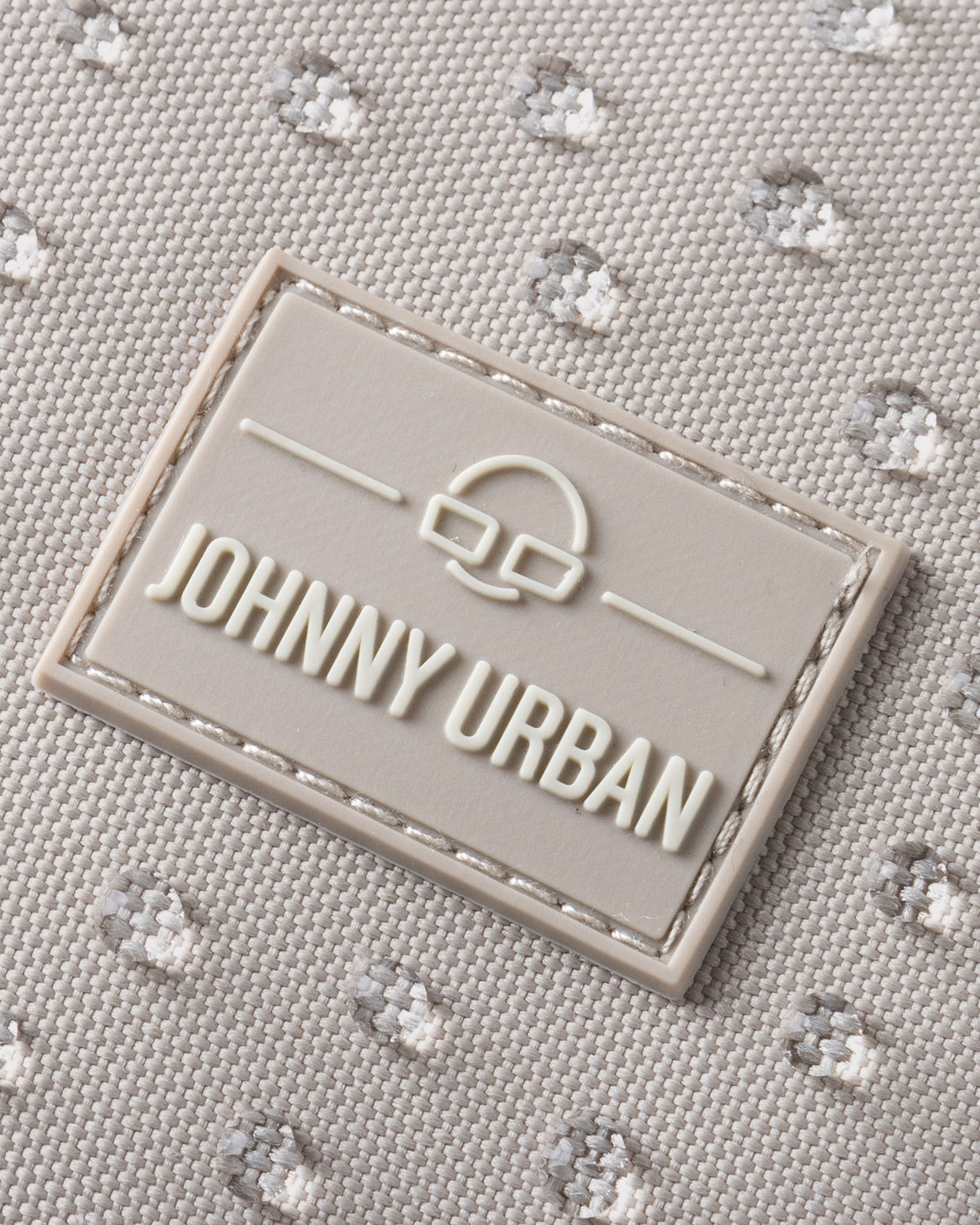 Nahaufnahme des wasserfesten sandfarbenen Rucksacks 'Mo' mit Johnny Urban Logo in einer rechteckigen Gummimarke