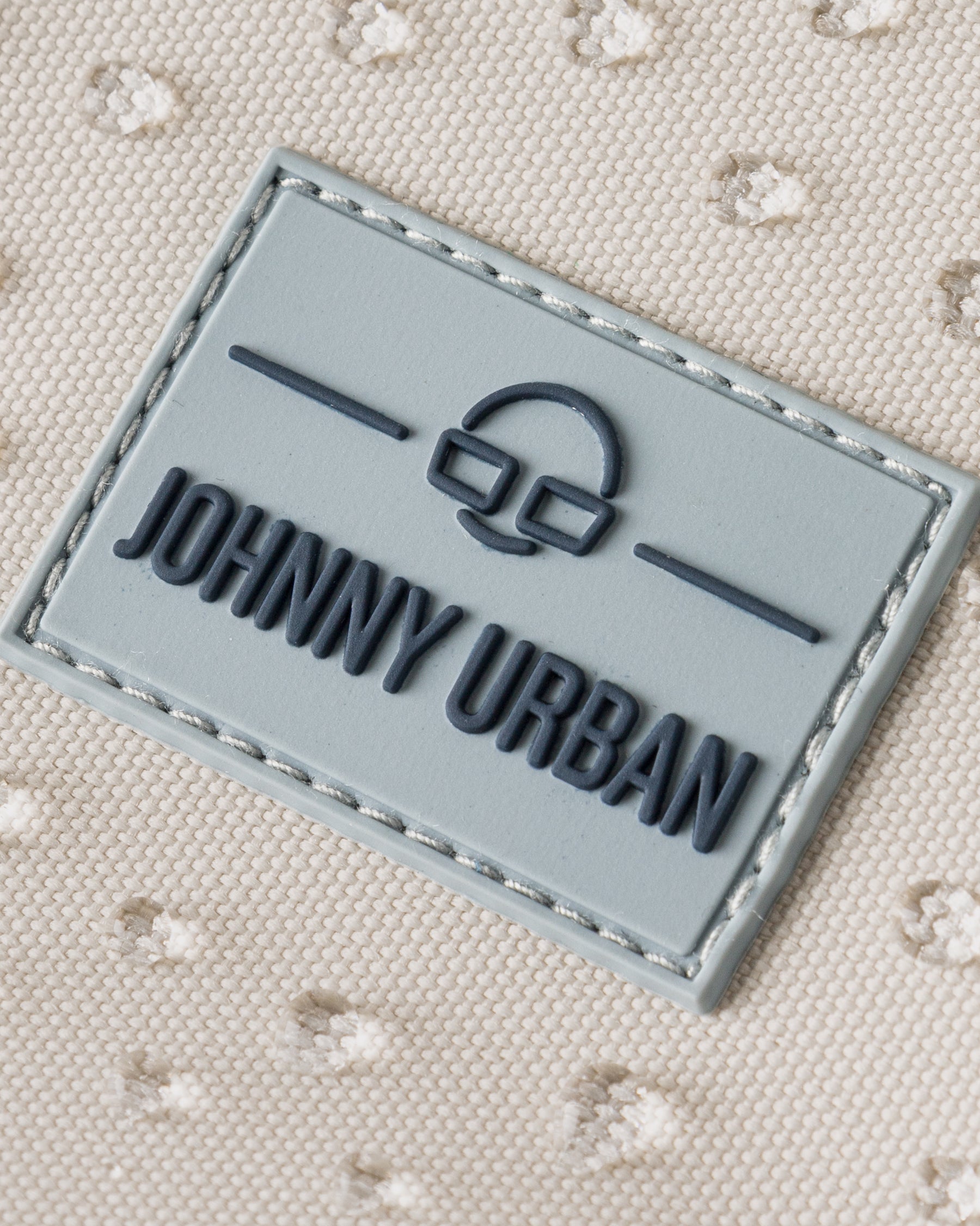 Nahaufnahme des Johnny Urban Logos auf dem sandfarbenen, wasserfesten Rucksack 'Mo' mit geprägtem Schild