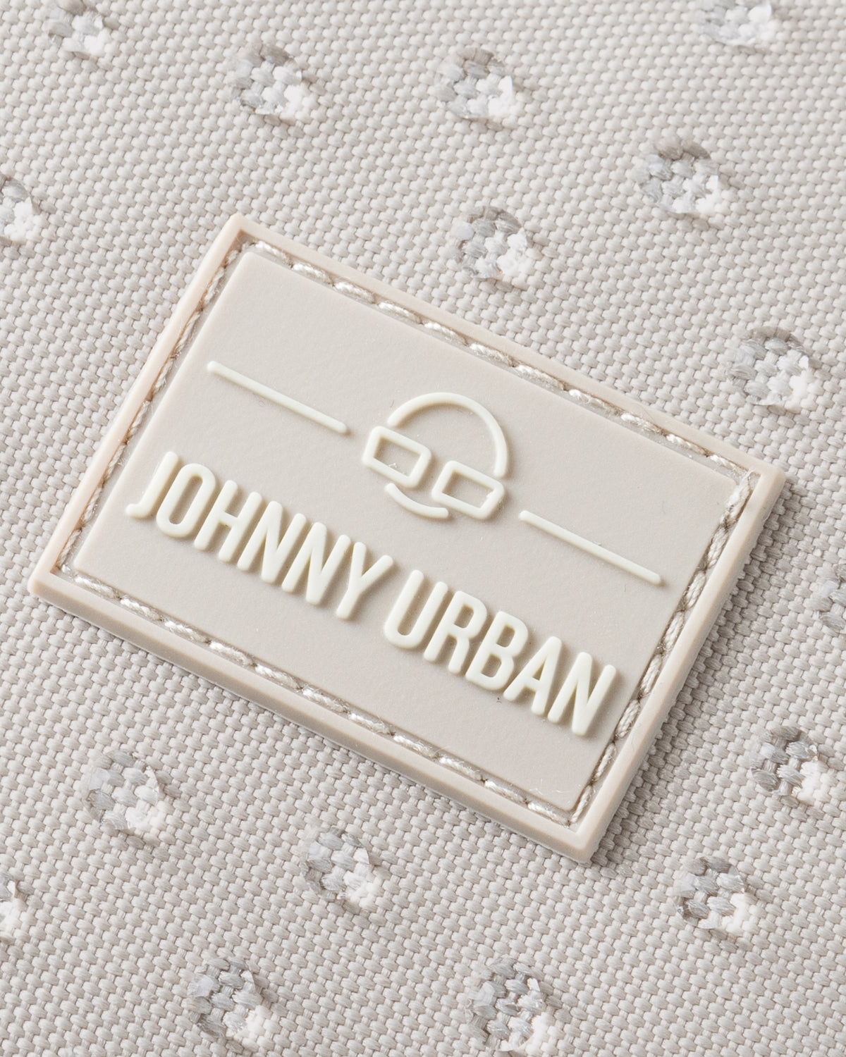 Nahaufnahme des Johnny Urban Logos auf sandfarbenem, wasserdichtem Rucksackstoff mit gepunkteter Struktur