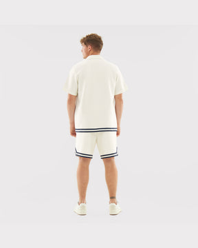 Mann trägt cremefarbenes Kurzarm-Set 'Parker' mit dunklen Streifen am Saum von Shirt und Shorts