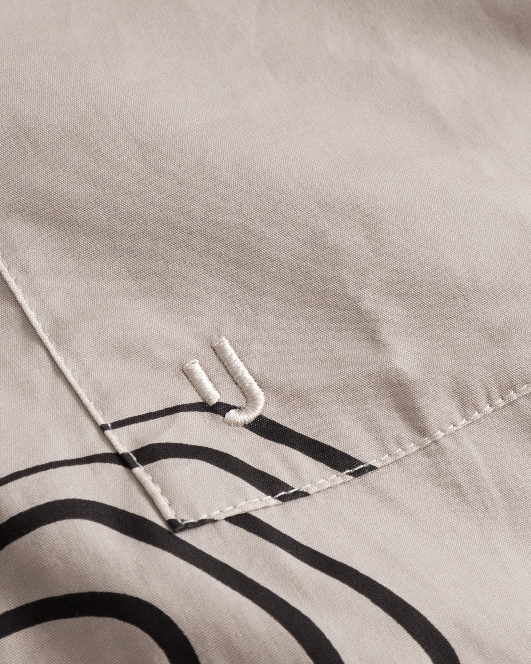 Sandfarbene Baumwolltasche mit schwarzem, abstraktem Linienmuster und gesticktem 'JU'-Logo