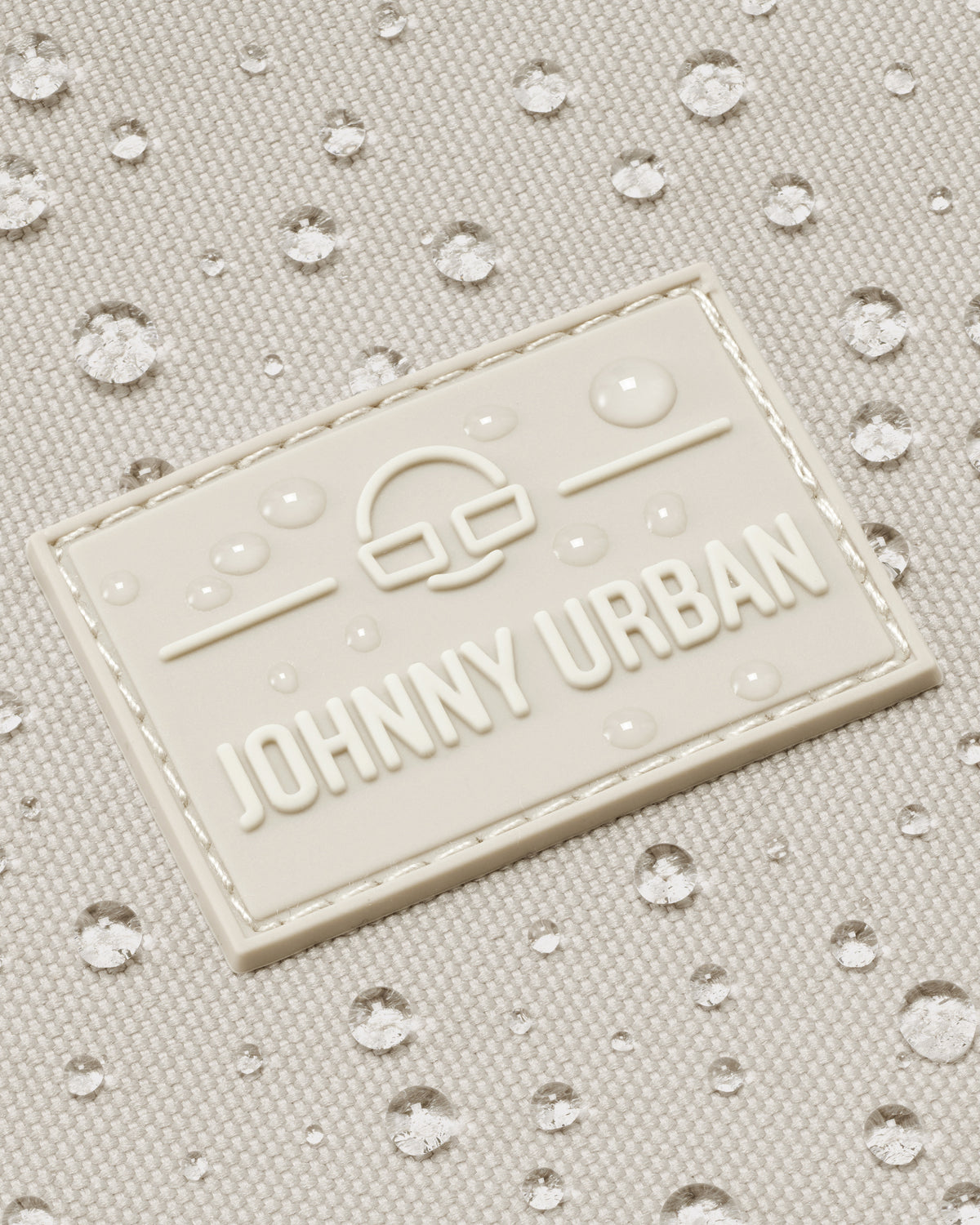 Nahaufnahme des wasserabweisenden Johnny Urban Logos auf sandfarbenem Shopper-Material mit Wassertropfen
