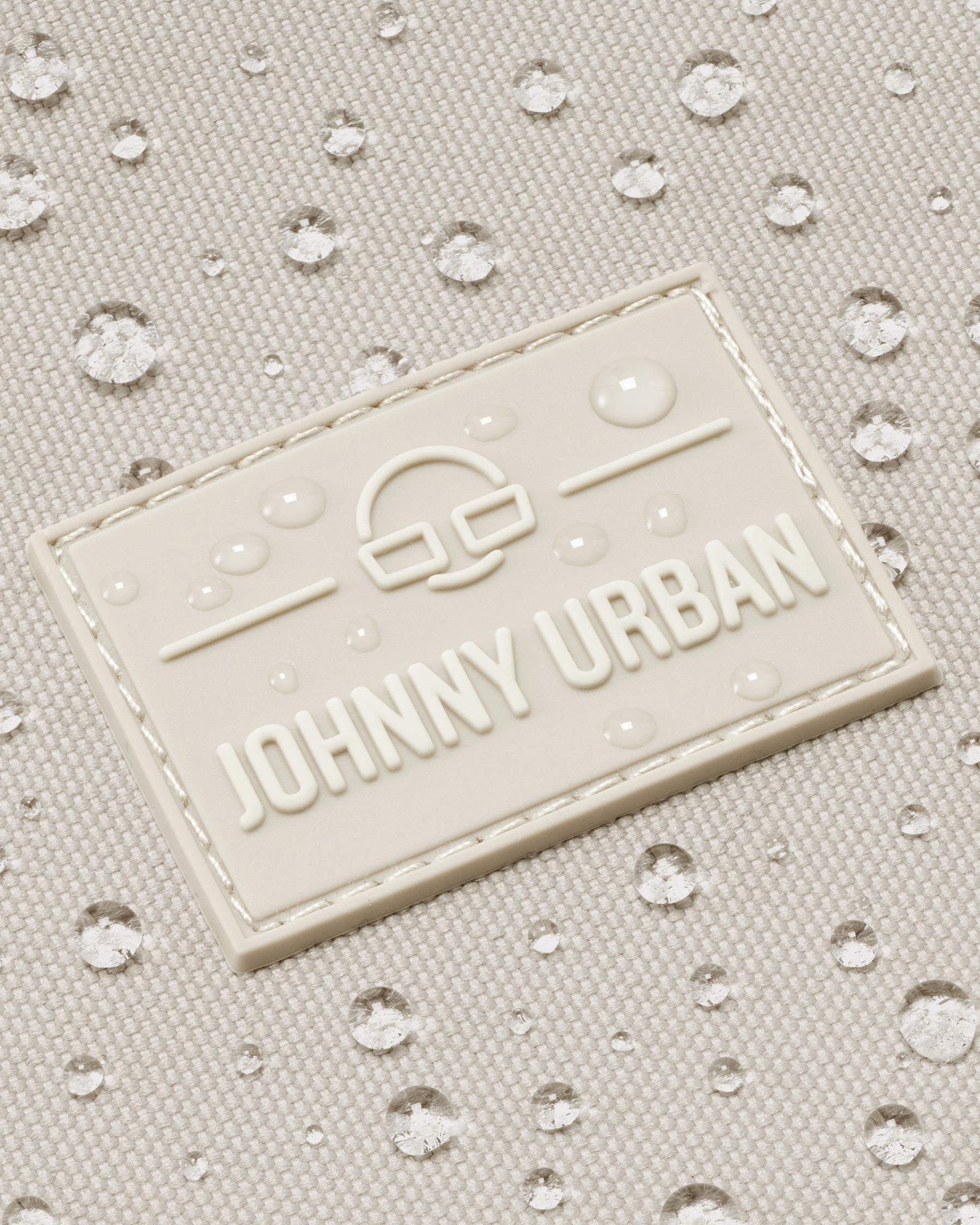 Nahaufnahme des wasserabweisenden Johnny Urban Logos auf sandfarbenem Shopper-Material mit Wassertropfen