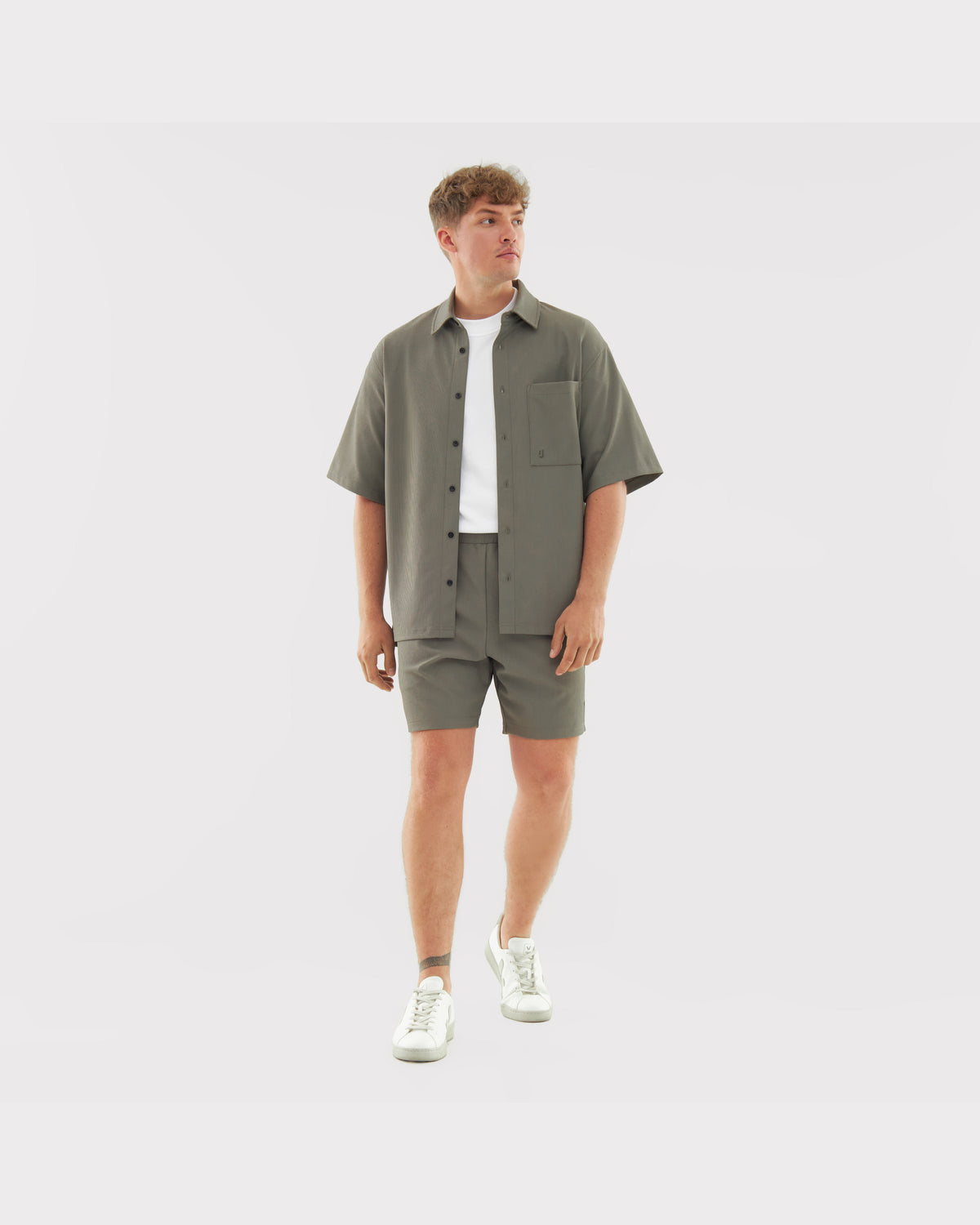 Männliches Model trägt olivegrüne Shorts 'Mason' und passende Hemdjacke mit weißem T-Shirt und weißen Sneakers