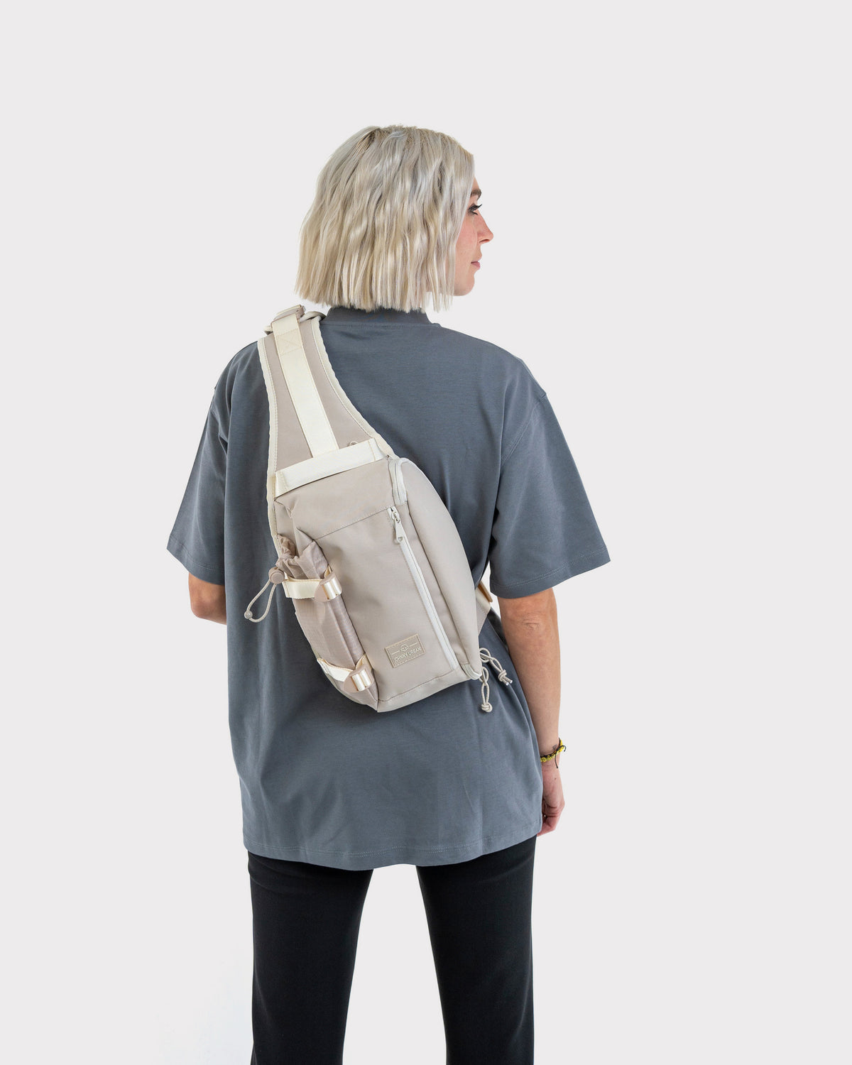 Beige Sling Bag 'Charlie' von Johnny Urban, getragen über den Rücken einer Person mit grauem T-Shirt und schwarzer Hose