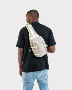 Mann trägt beigen Johnny Urban Sling Bag 'Charlie' quer am Rücken über schwarzem T-Shirt und blauen Jeans
