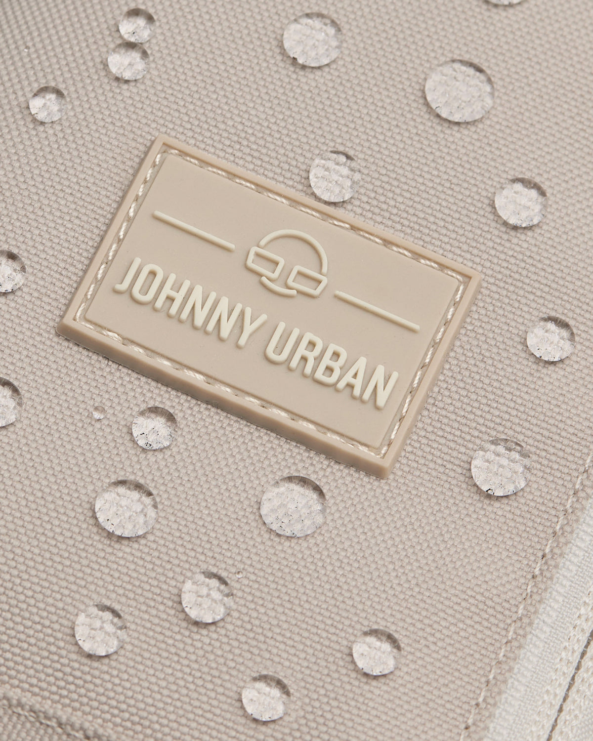 Nahaufnahme der beigen wasserabweisenden Oberfläche der Johnny Urban Sling Bag Charlie mit Wassertropfen