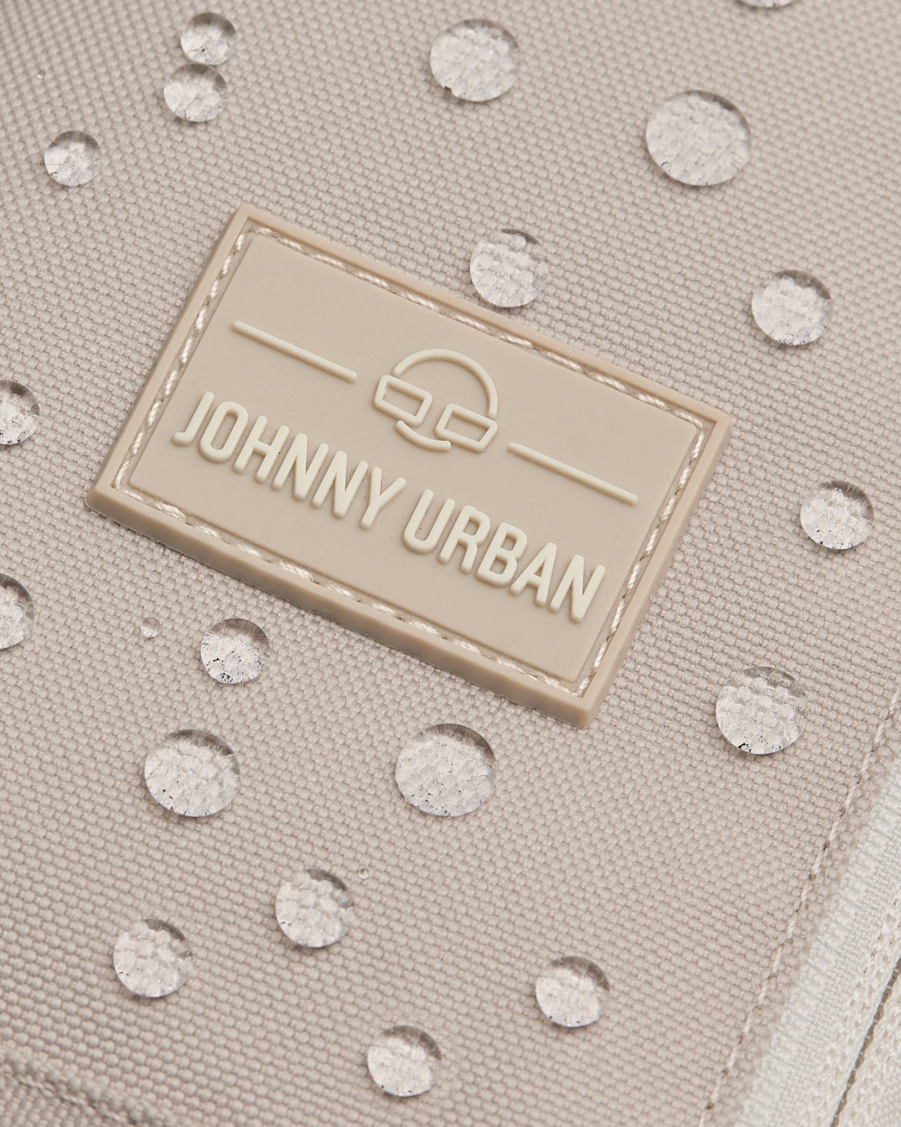 Nahaufnahme der beigen wasserabweisenden Oberfläche der Johnny Urban Sling Bag Charlie mit Wassertropfen