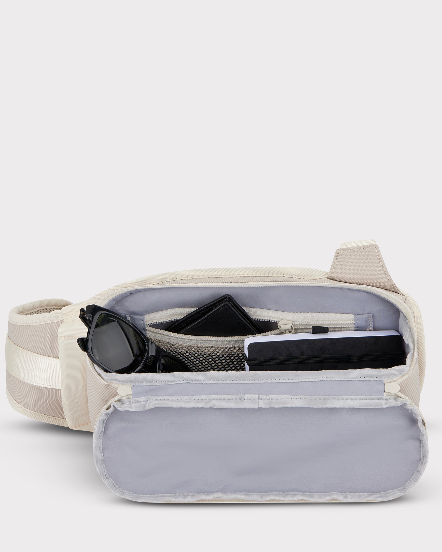 Offene sandfarbene Johnny Urban Sling Bag 'Charlie' mit Sonnenbrille, Geldbörse und Notizbuch