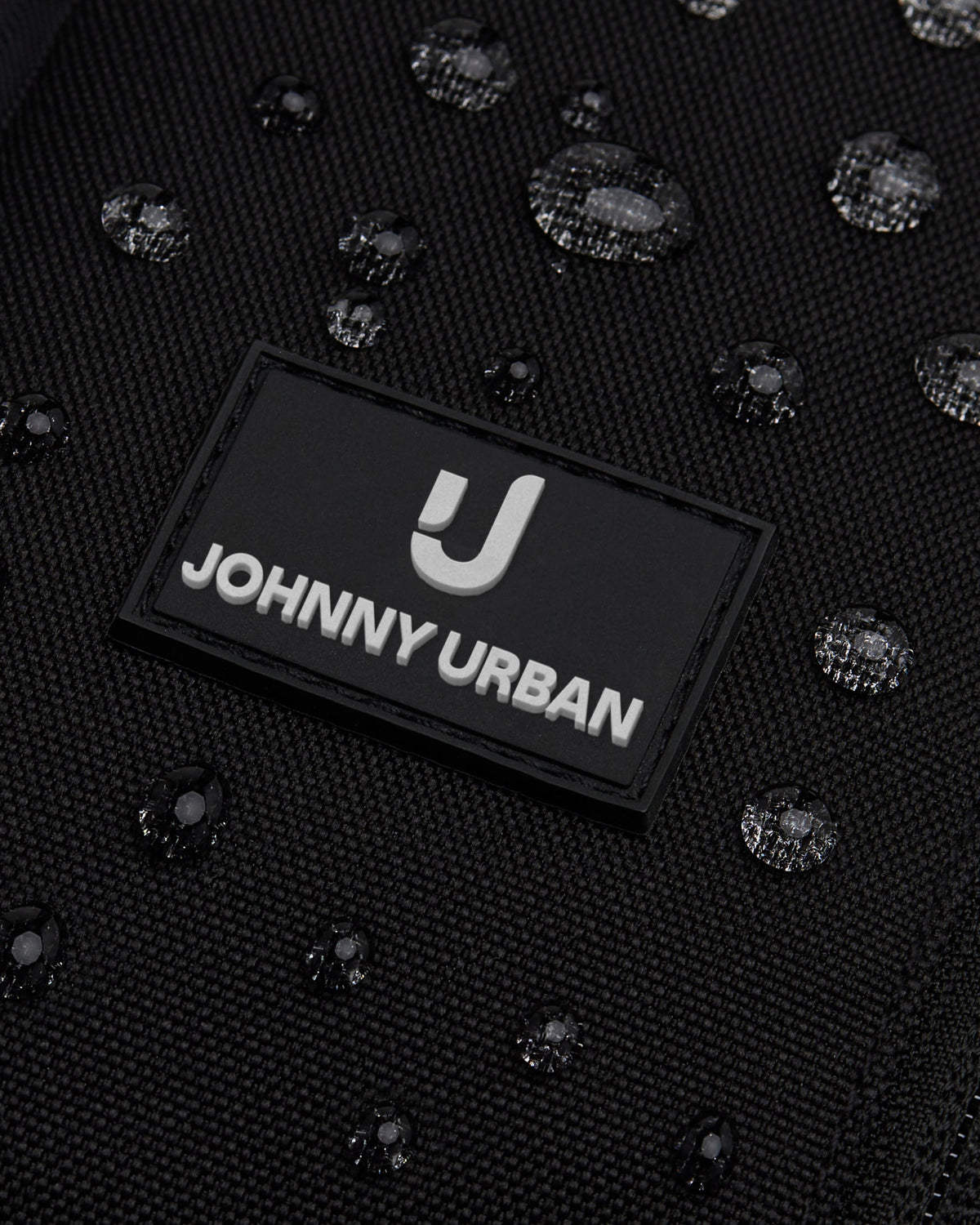 Nahe Nahaufnahme des schwarzen wasserabweisenden Sling Bags 'Charlie' von Johnny Urban mit sichtbaren Wassertropfen