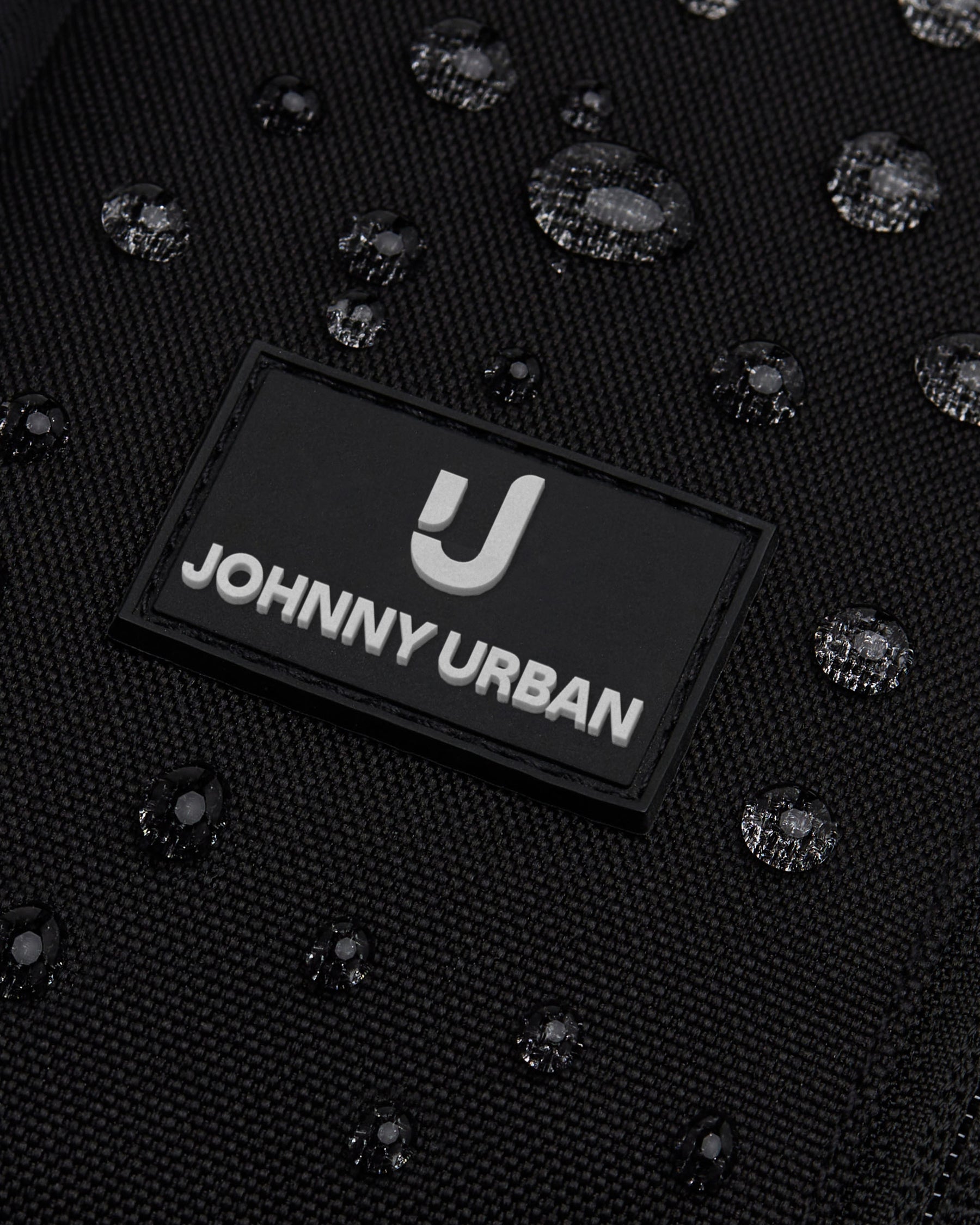 Nahe Nahaufnahme des schwarzen wasserabweisenden Sling Bags 'Charlie' von Johnny Urban mit sichtbaren Wassertropfen