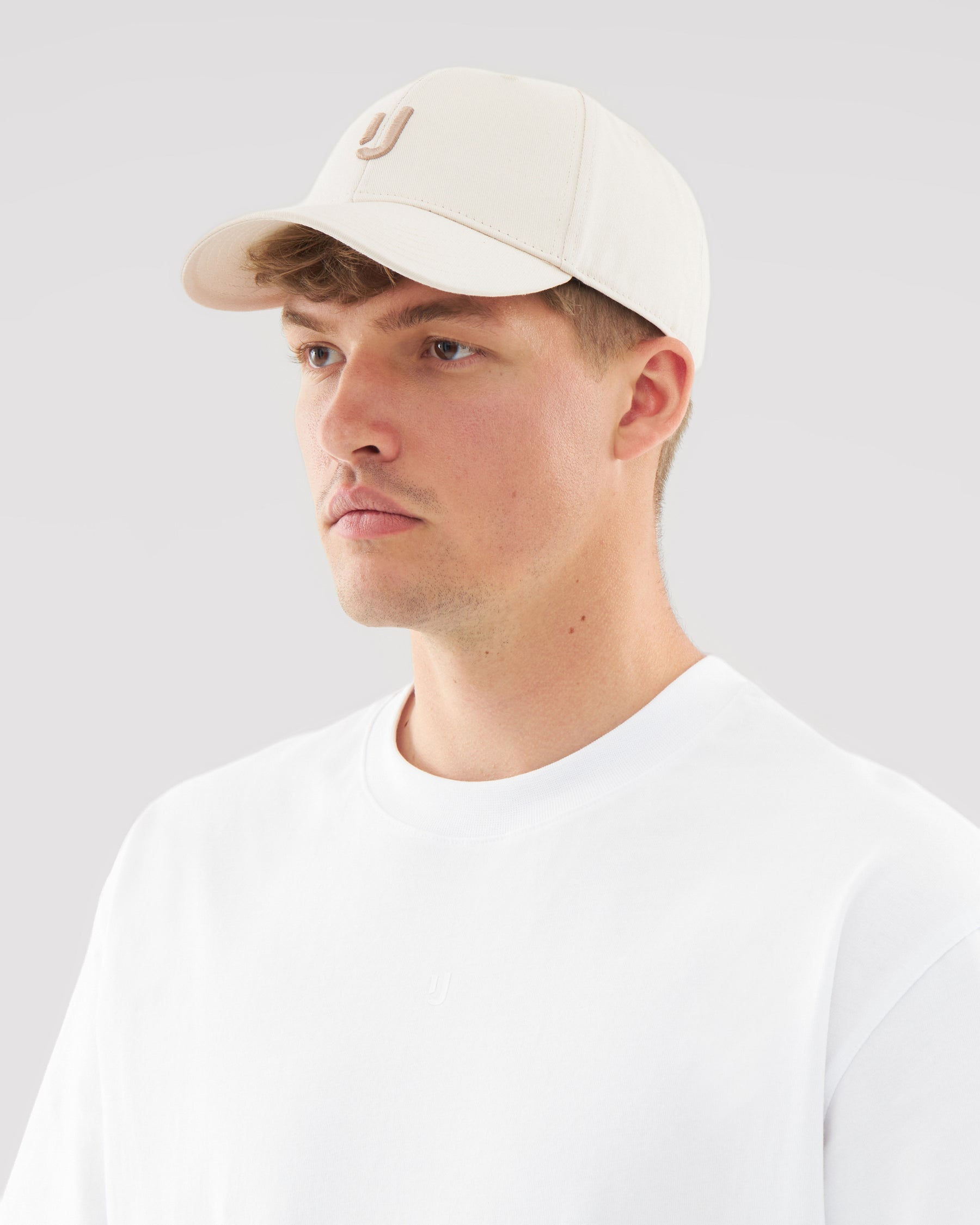 Mann trägt cremefarbene Snapback-Cap 'Jason' mit aufgesticktem J und weißes T-Shirt