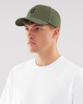 Mann trägt olivgrüne Snapback-Cap 'Jason' mit schwarzem Logo und weißem T-Shirt