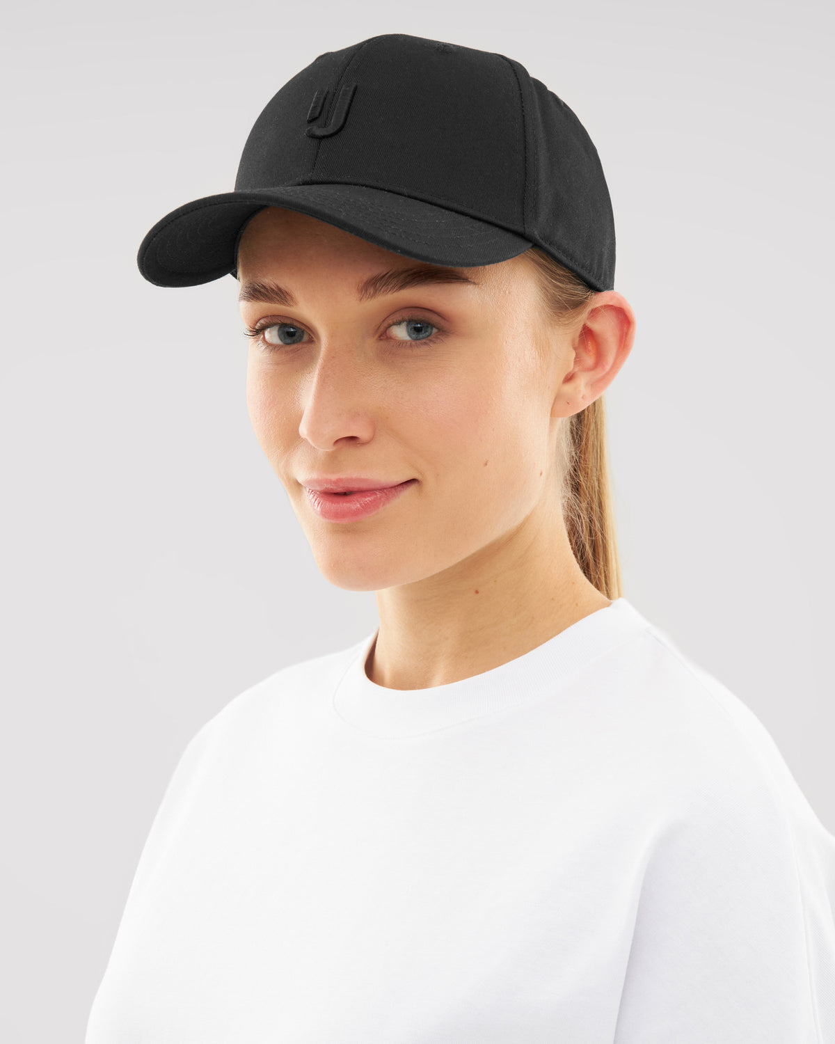 Frau trägt schwarzen Snapback Cap 'Jason' mit dezentem 'J'-Logo, weiße Shirt