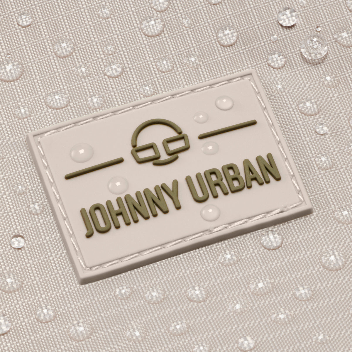 Nahaufnahme des Johnny Urban Logos auf einem beigen Duffle Bag mit Wassertropfen