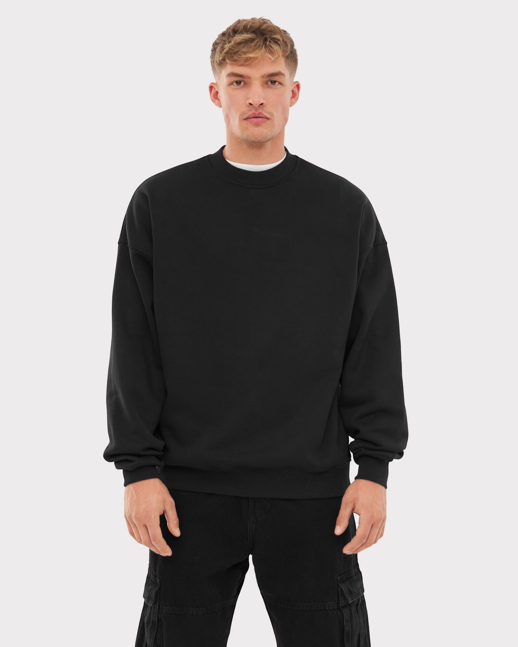Mann trägt schwarzen oversized Crewneck Pullover 'Carter' und schwarze Cargo-Hose