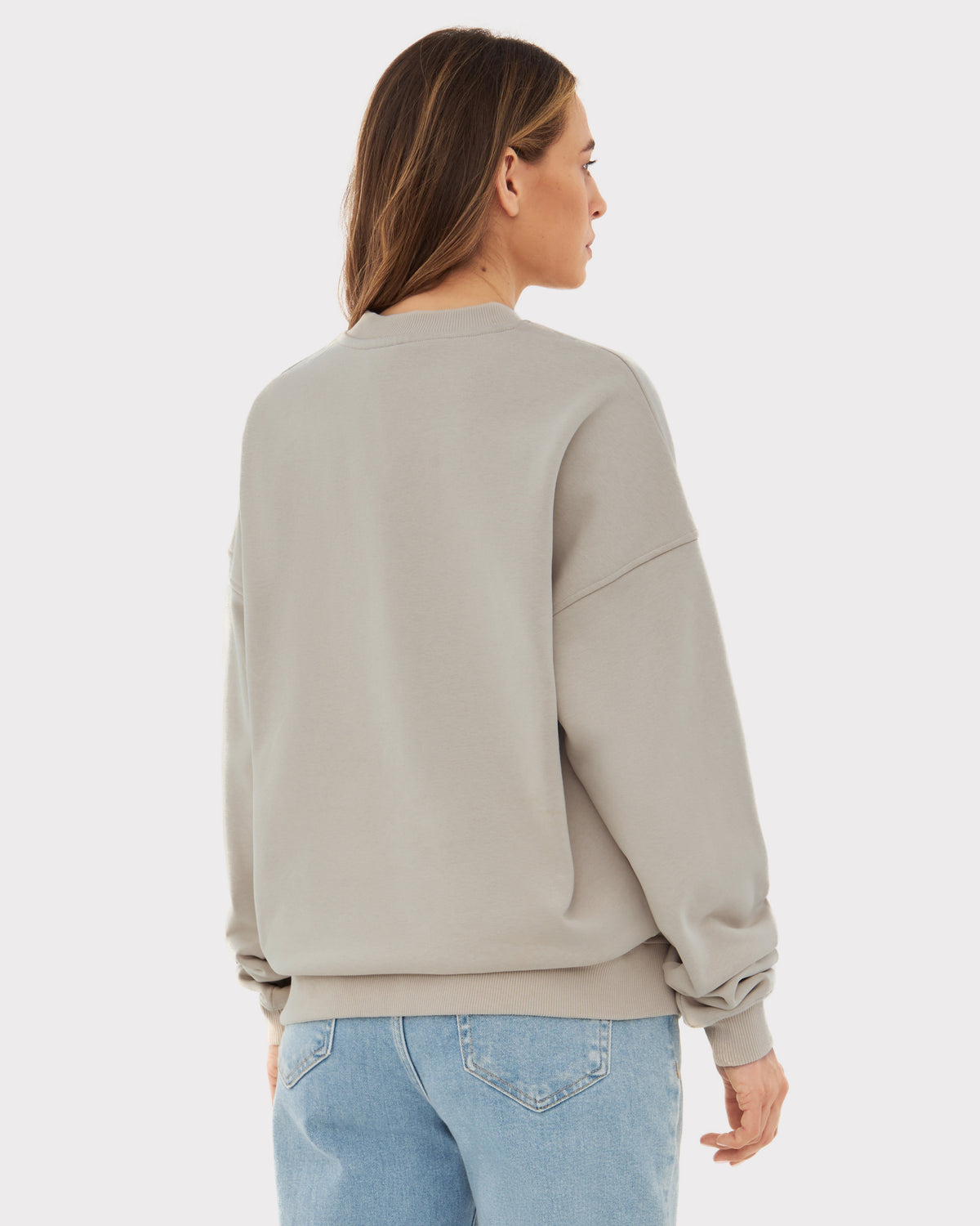Damen trägt oversized Crewneck 'Carter' Pullover in Beige von hinten mit hellblauen Jeans