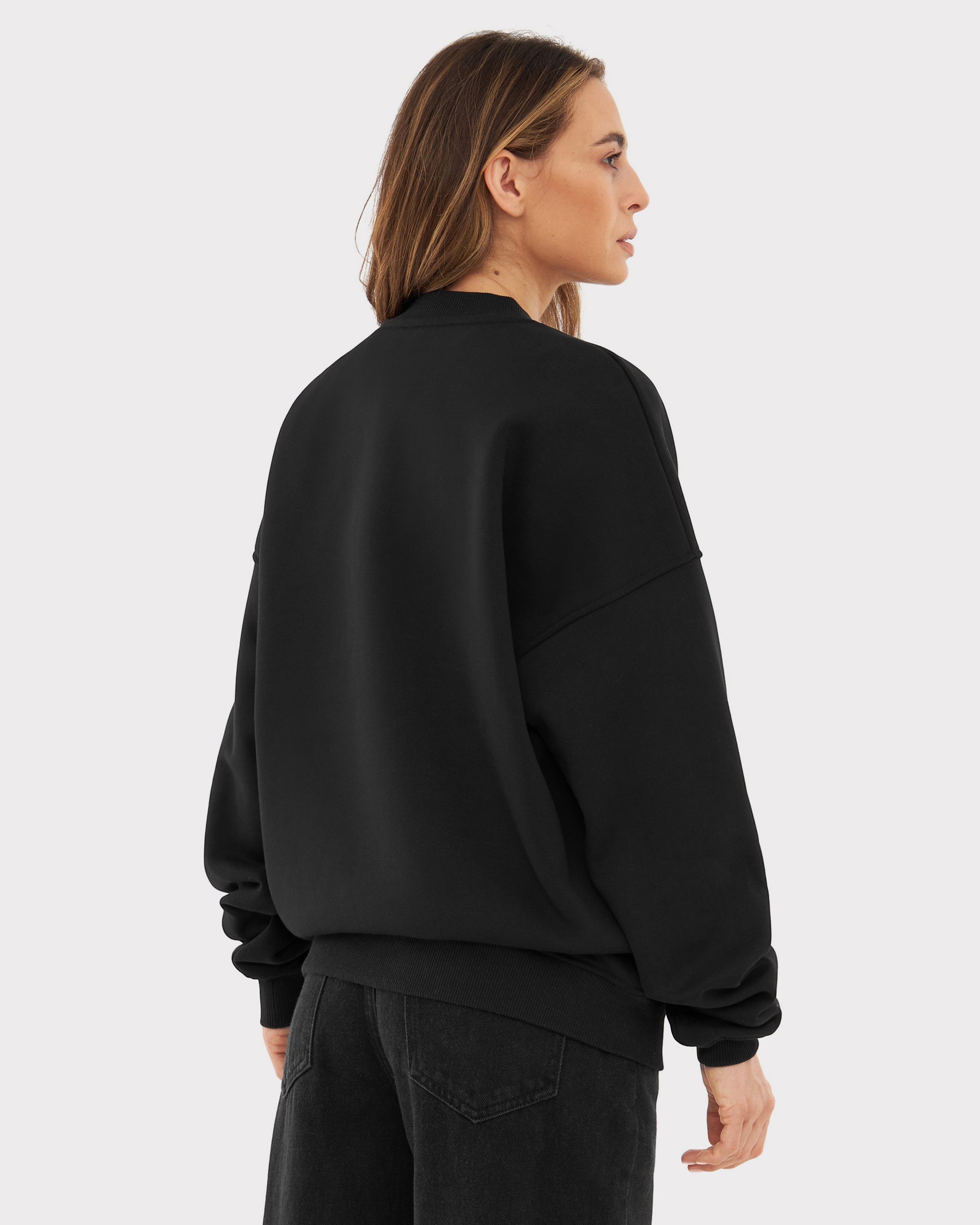 Dame von hinten mit oversized schwarzem Crewneck 'Carter' und schwarzen Jeans