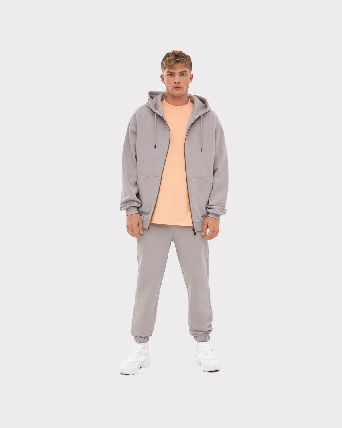 Mann trägt graue Jogginghose 'Owen', grauen Hoodie und helloranges T-Shirt