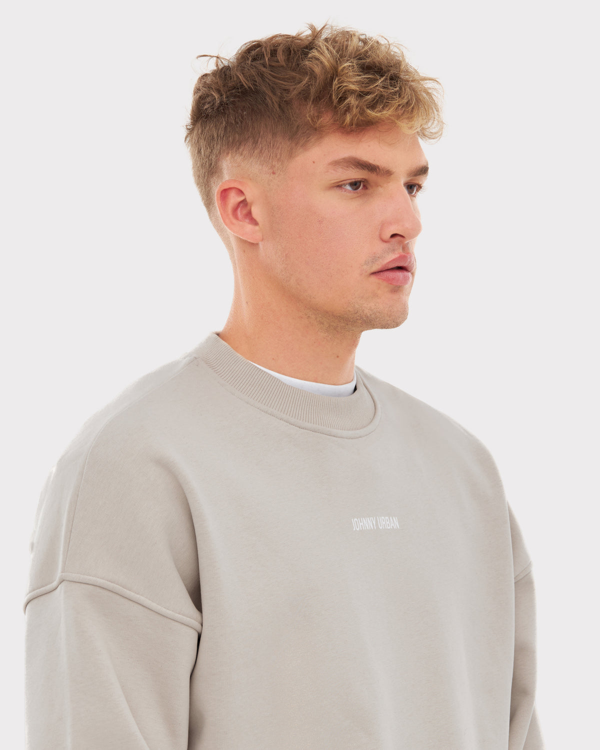 Mann trägt oversized Crewneck 'Carter' von Johnny Urban in Beige mit kleinem weißen Markenlogo auf der Brust