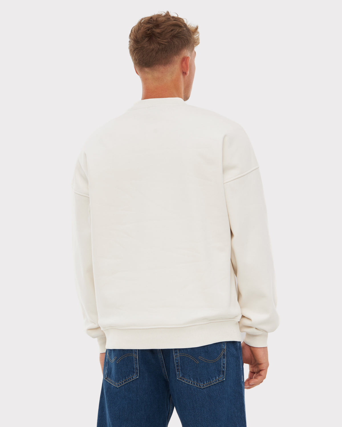 Rückansicht eines Mannes mit oversized weißen Johnny Urban Crewneck 'Carter' und blauen Jeans