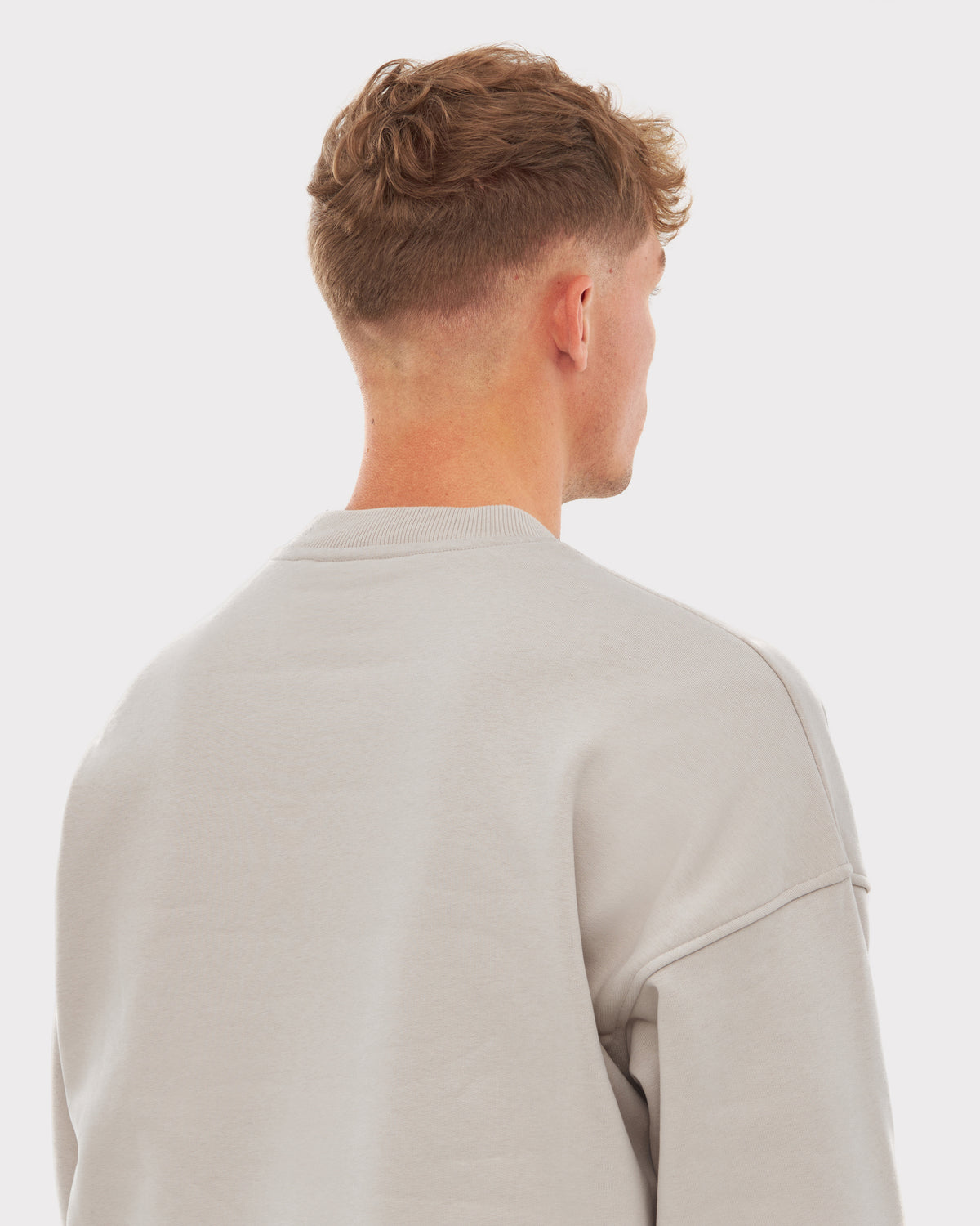Rückansicht eines Mannes mit kurzem, lockigem Haar, der einen beigefarbenen Oversized Crewneck 'Carter' trägt