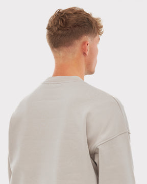 Rückansicht eines Mannes mit kurzem, lockigem Haar, der einen beigefarbenen Oversized Crewneck 'Carter' trägt