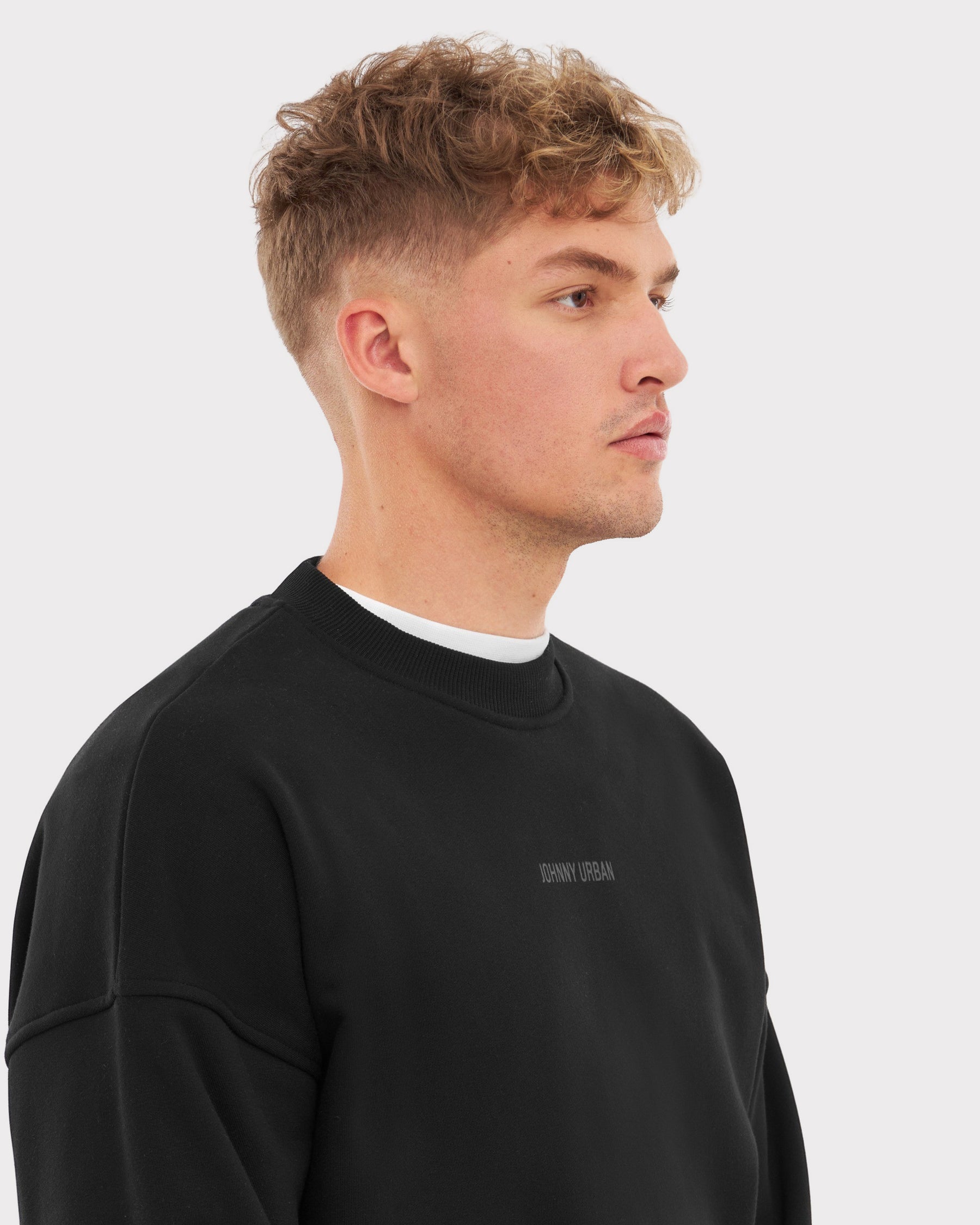 Mann trägt schwarzen Oversized Crewneck 'Carter' Sweatshirt mit kleinem 'Johnny Urban' Print vorne