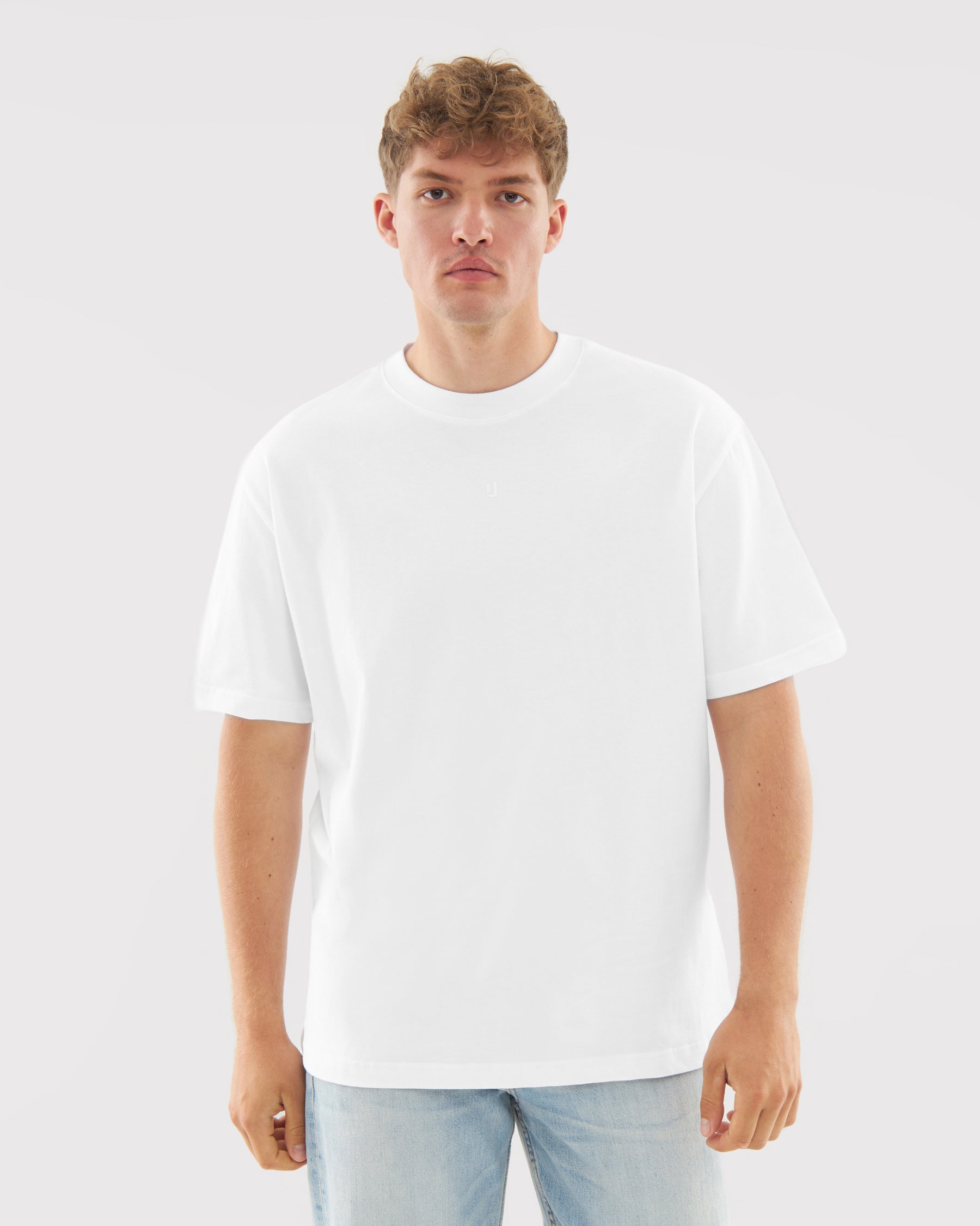 Mann mit neutralem Gesichtsausdruck trägt weißes T-Shirt "Sammy Butterfly" und helle Jeans