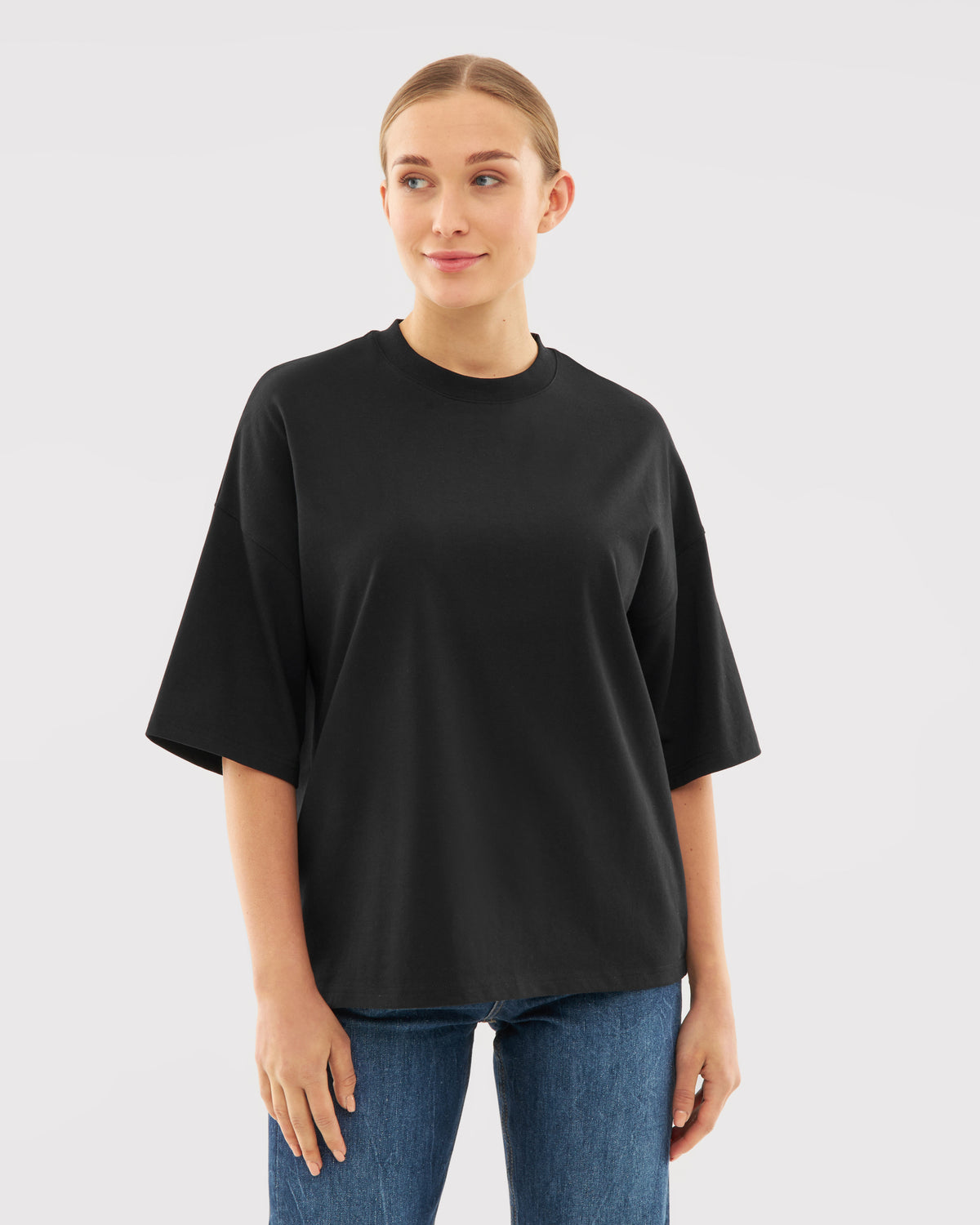 Frau trägt schwarzes Oversize-T-Shirt 'Vic' mit kurzen Ärmeln und blauer Jeans