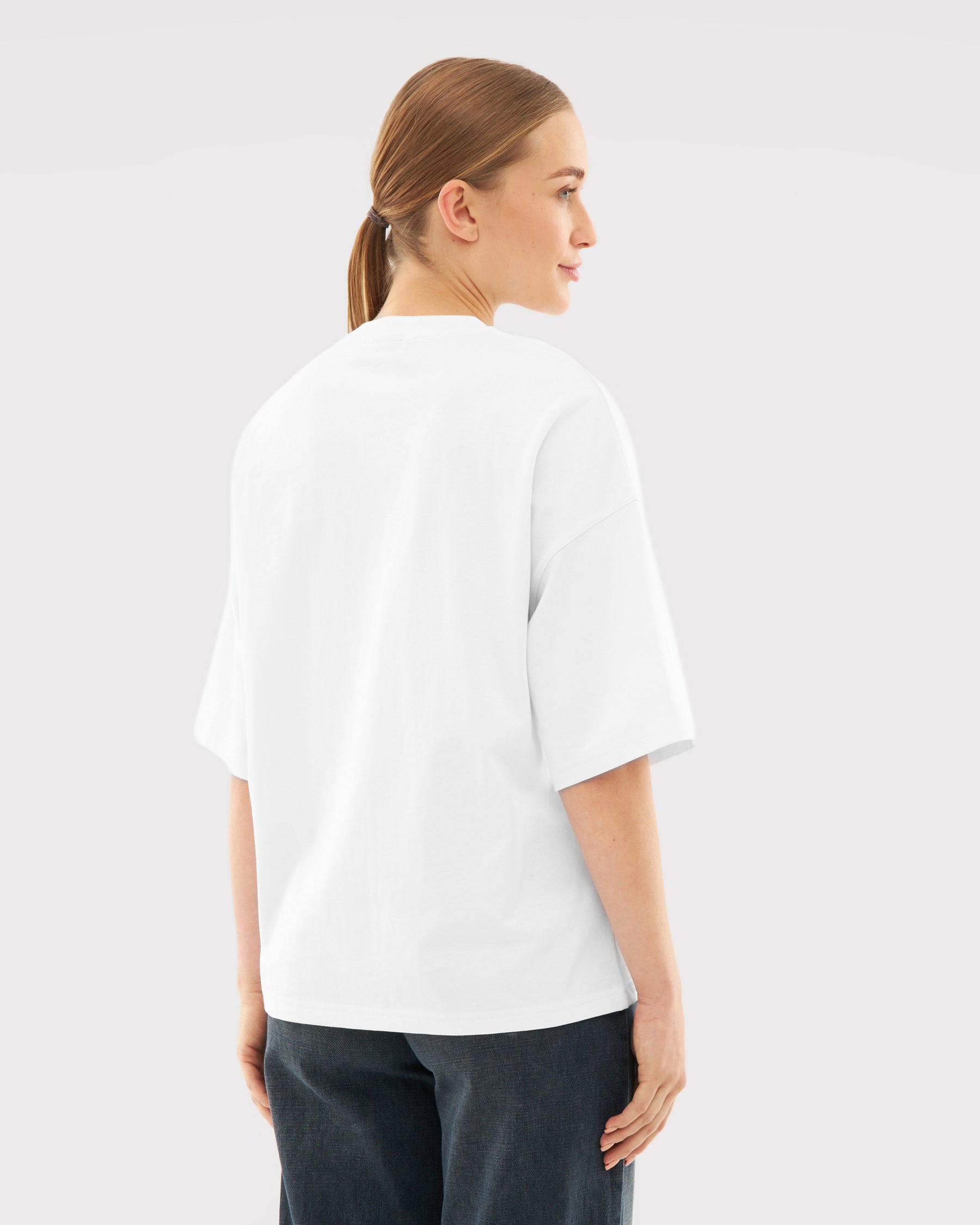 Frau trägt weißes Oversize-T-Shirt 'Vic' von hinten mit dunkler Hose