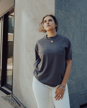 Frau trägt das graue Oversize T-Shirt 'Sammy' von Johnny Urban und weiße Hosen, steht vor einer grauen Steinwand