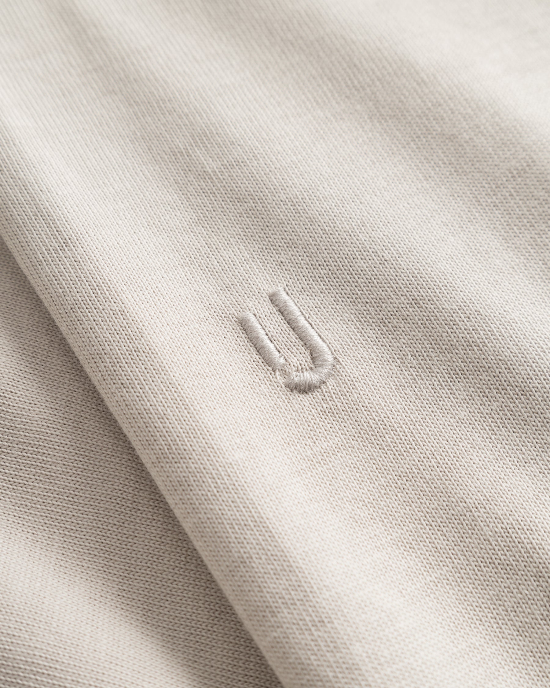Nahaufnahme des beigen Stoffs eines Oversize-T-Shirts 'Vic' mit eingesticktem Detail