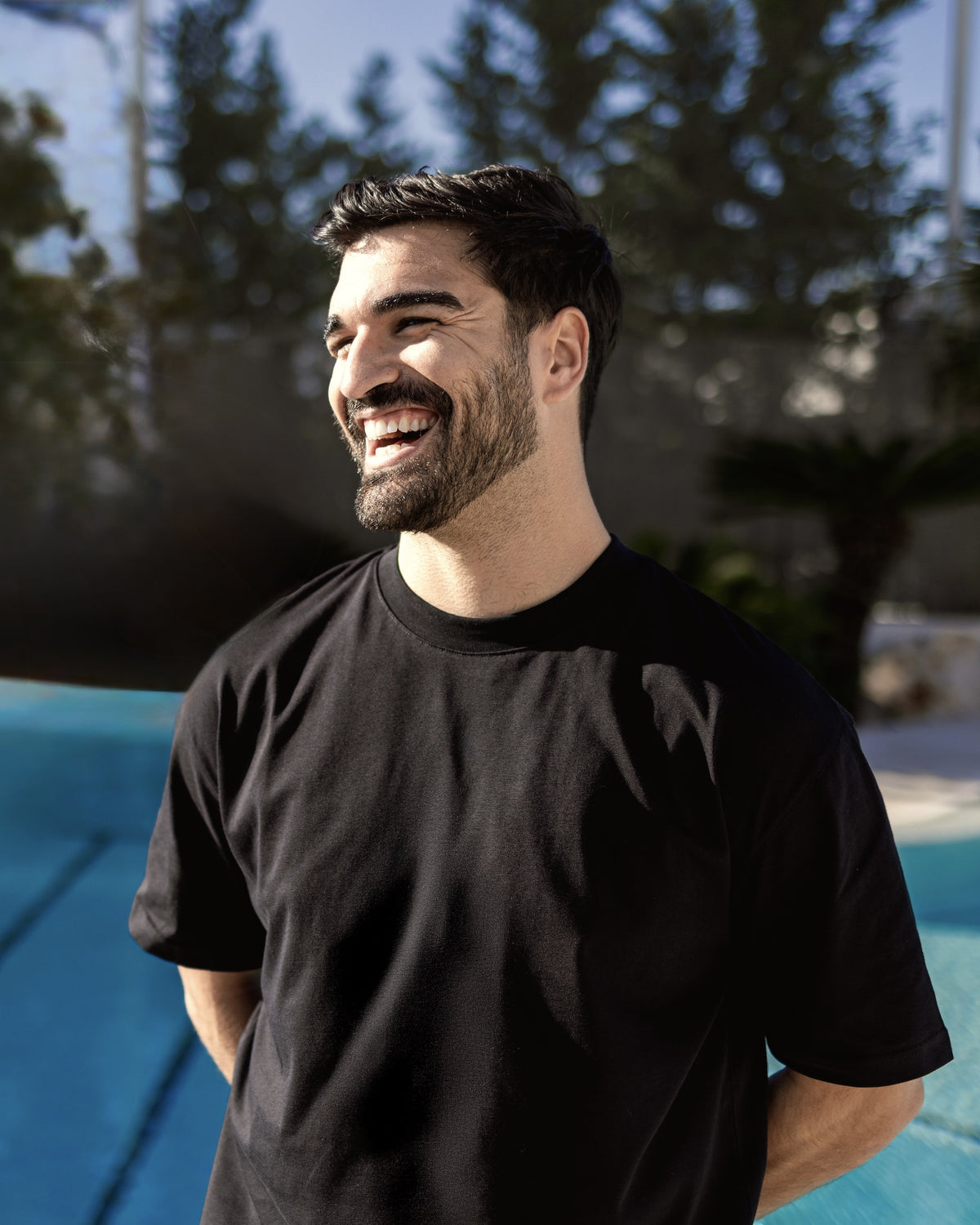 Mann trägt schwarzes Oversize-T-Shirt 'Vic' vor einem Pool