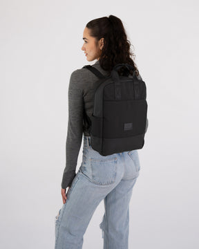 Frau mit schwarzem Johnny Urban Rucksack 'Jona Medium' trägt grauen Pullover und helle Jeans